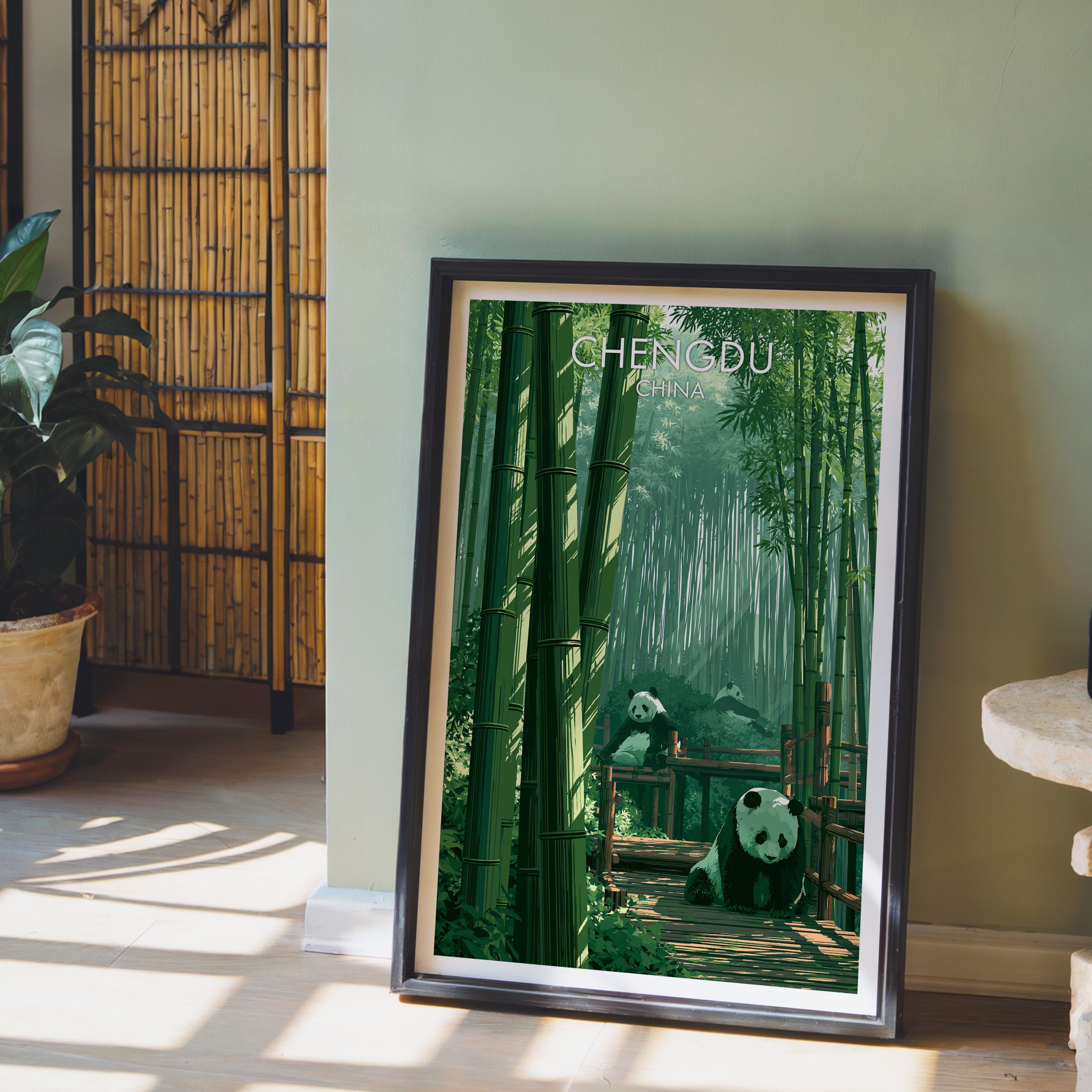 Giant Pandas Chengdu China wall art in a black frame leaning against a sage green wall beside a bamboo screen