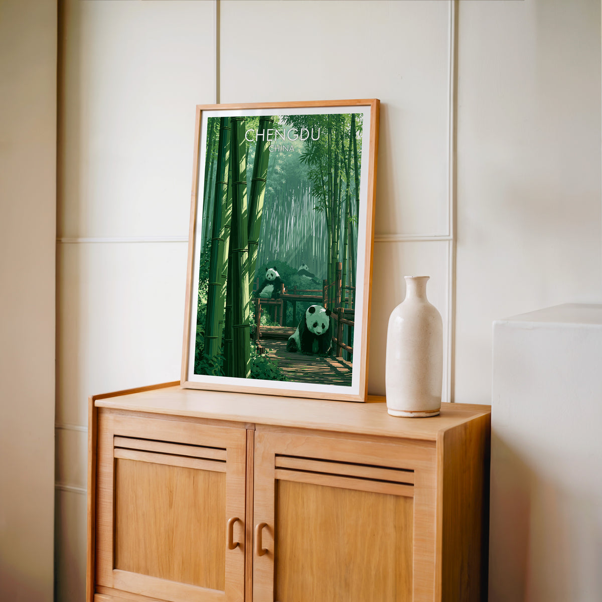 Chengdu giant panda travel poster in an oak frame standing on a light oak cabinet against a cream panelled wall