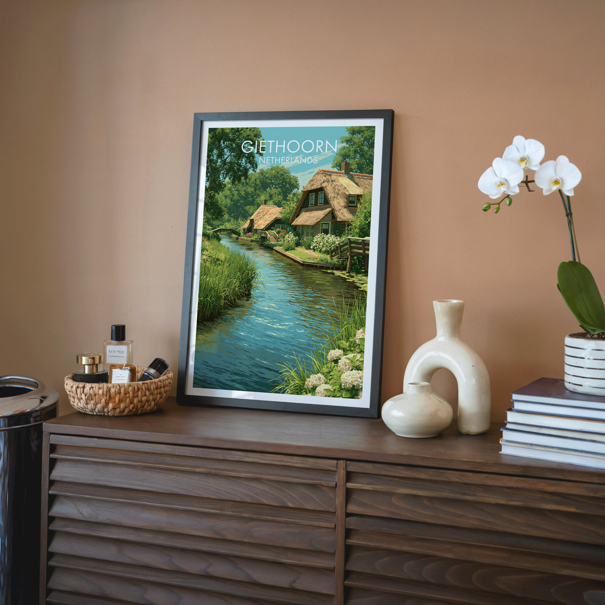 Dutch village wall art, black frame on a walnut sideboard against a terracotta wall with an orchid