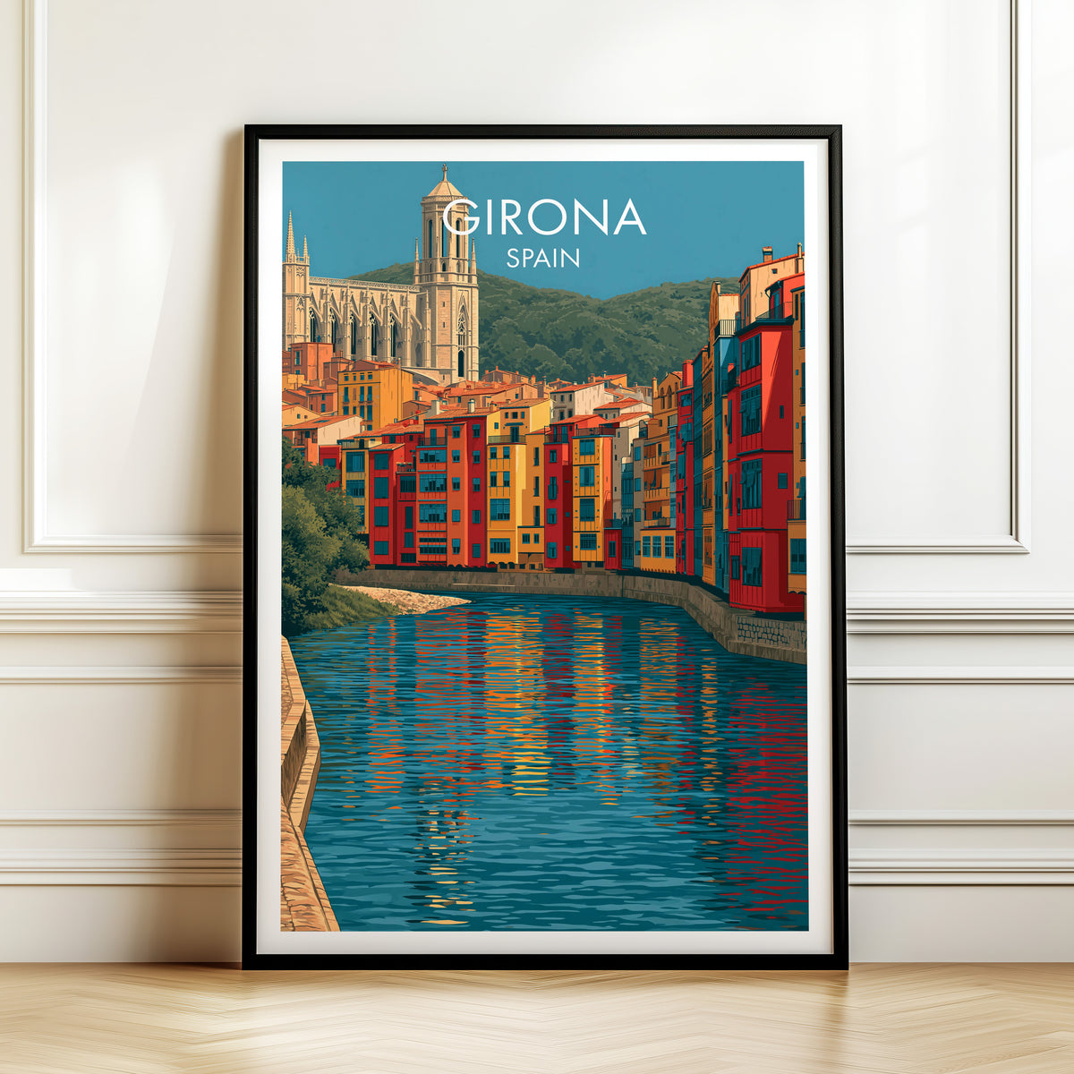 Girona coloured river houses print, black frame leaning on a white panelled wall above a herringbone floor