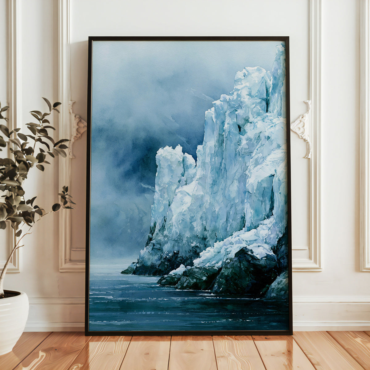 Glacier Bay National Park watercolor print in a black frame leaning against a white paneled wall beside a potted plant