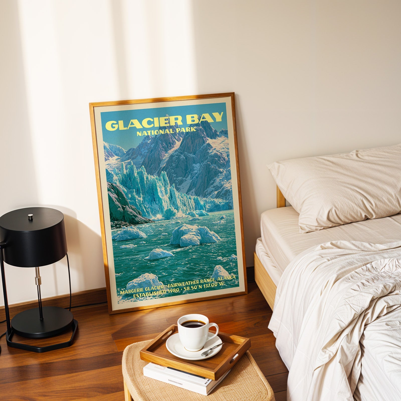 Margerie Glacier poster in a gold frame on the floor beside a made bed and a black table lamp