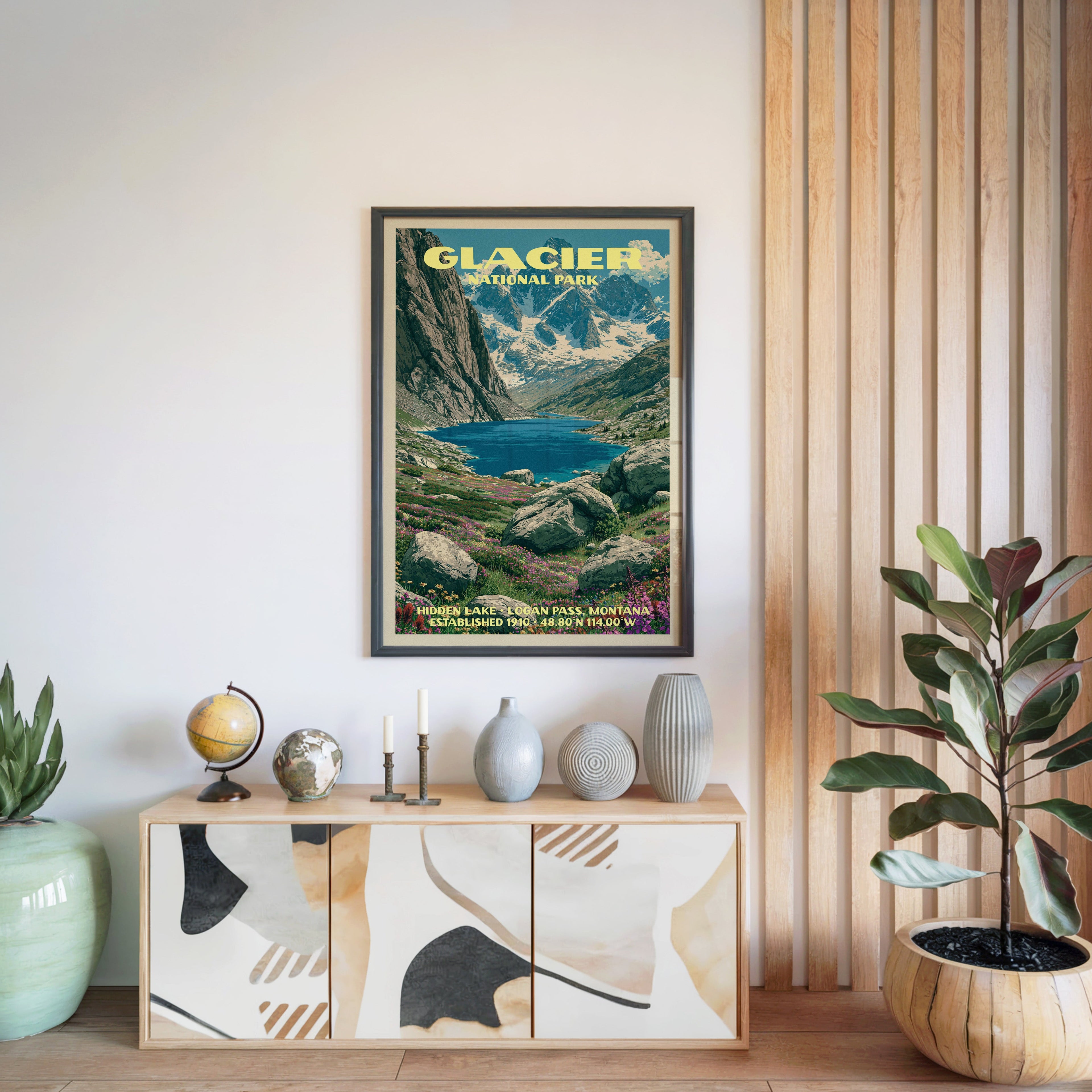Glacier National Park poster in a black frame above a light wood sideboard beside a slatted wall panel