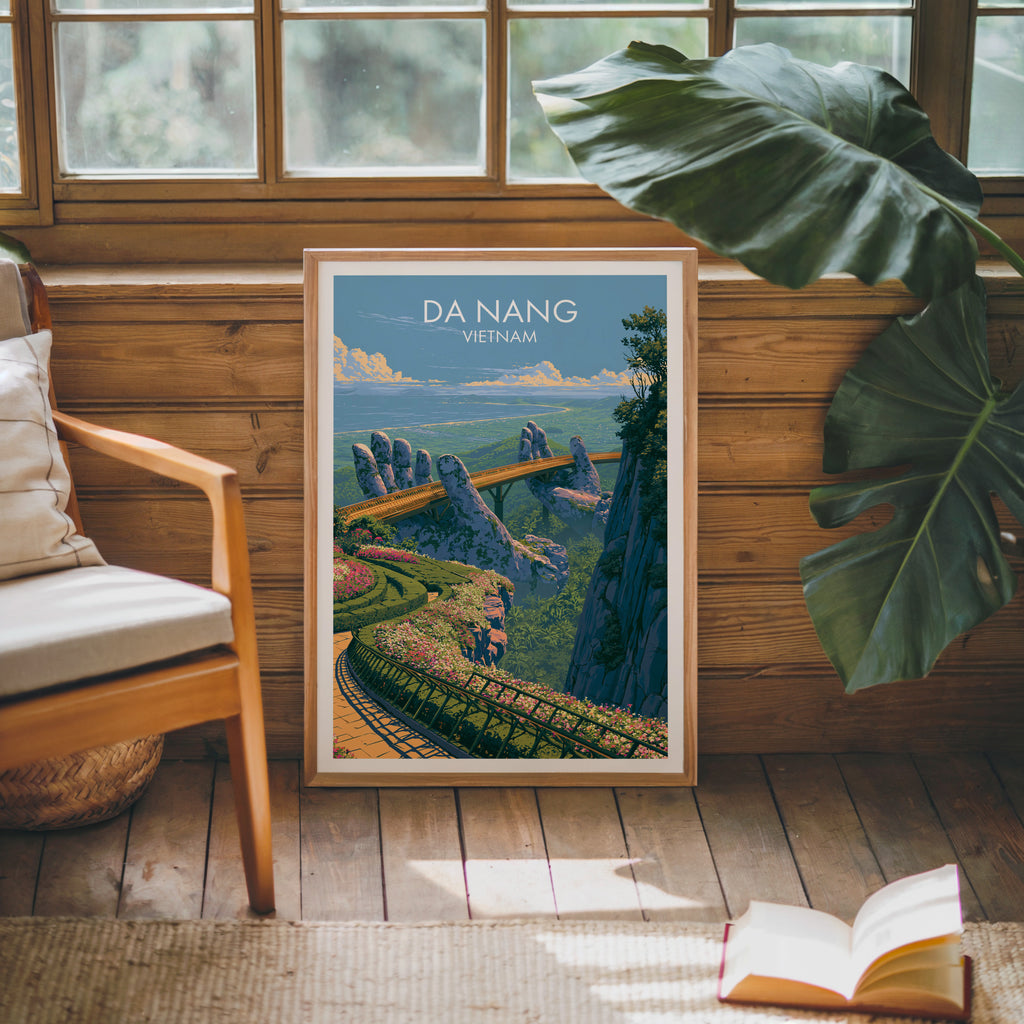 Framed Golden Bridge Da Nang Vietnam poster leaning against a timber cabin wall with monstera leaves and an open book