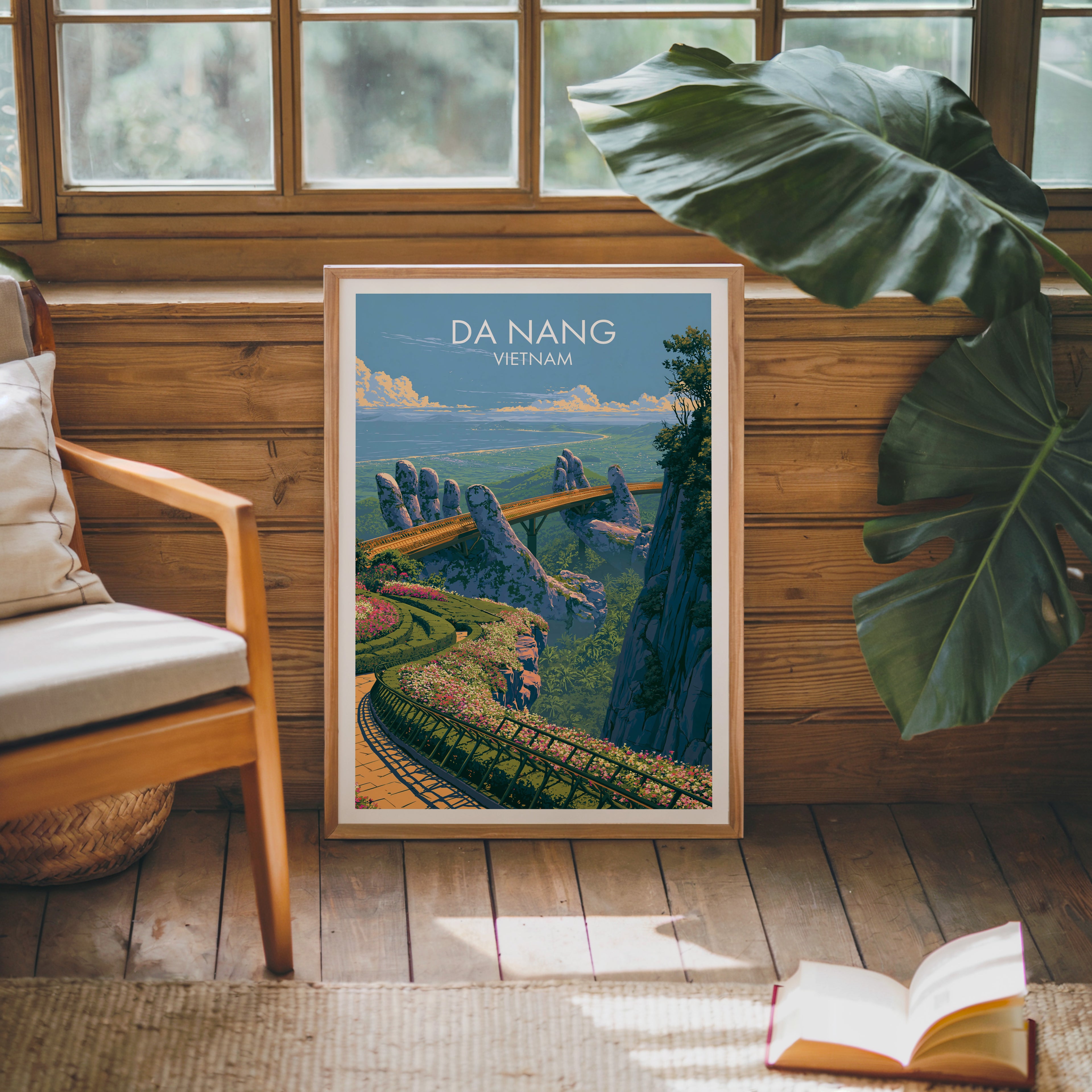 Framed Golden Bridge Da Nang Vietnam poster leaning against a timber cabin wall with monstera leaves and an open book