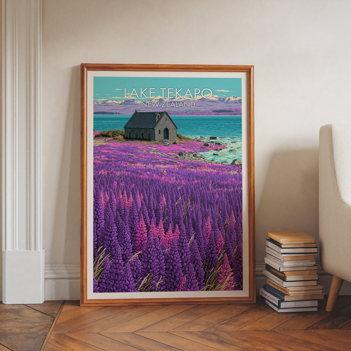 Lake Tekapo artwork in a walnut frame on herringbone floor beside stacked books and an armchair