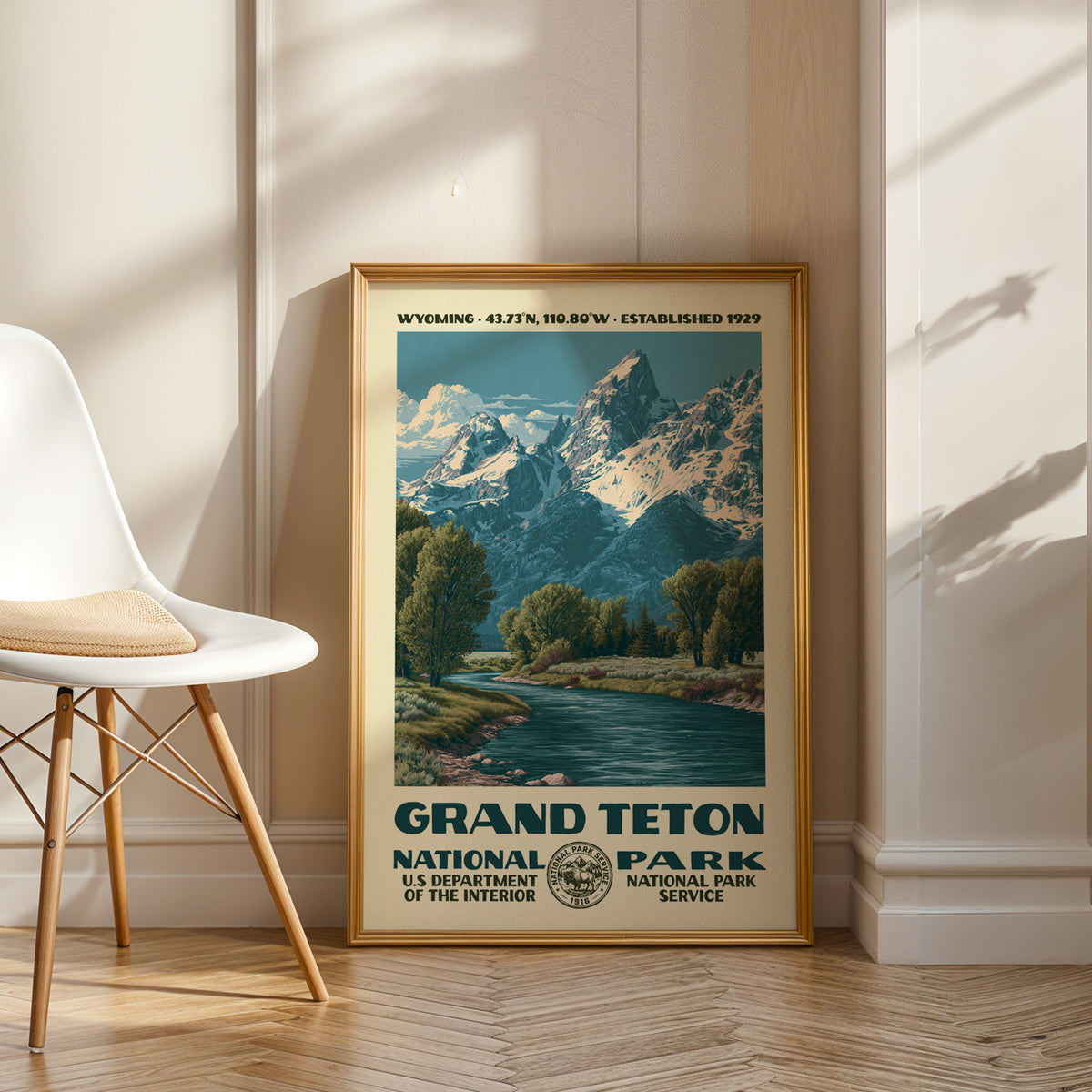 Grand Teton National Park vintage WPA art in an oak frame leaning by a white chair on a wood floor