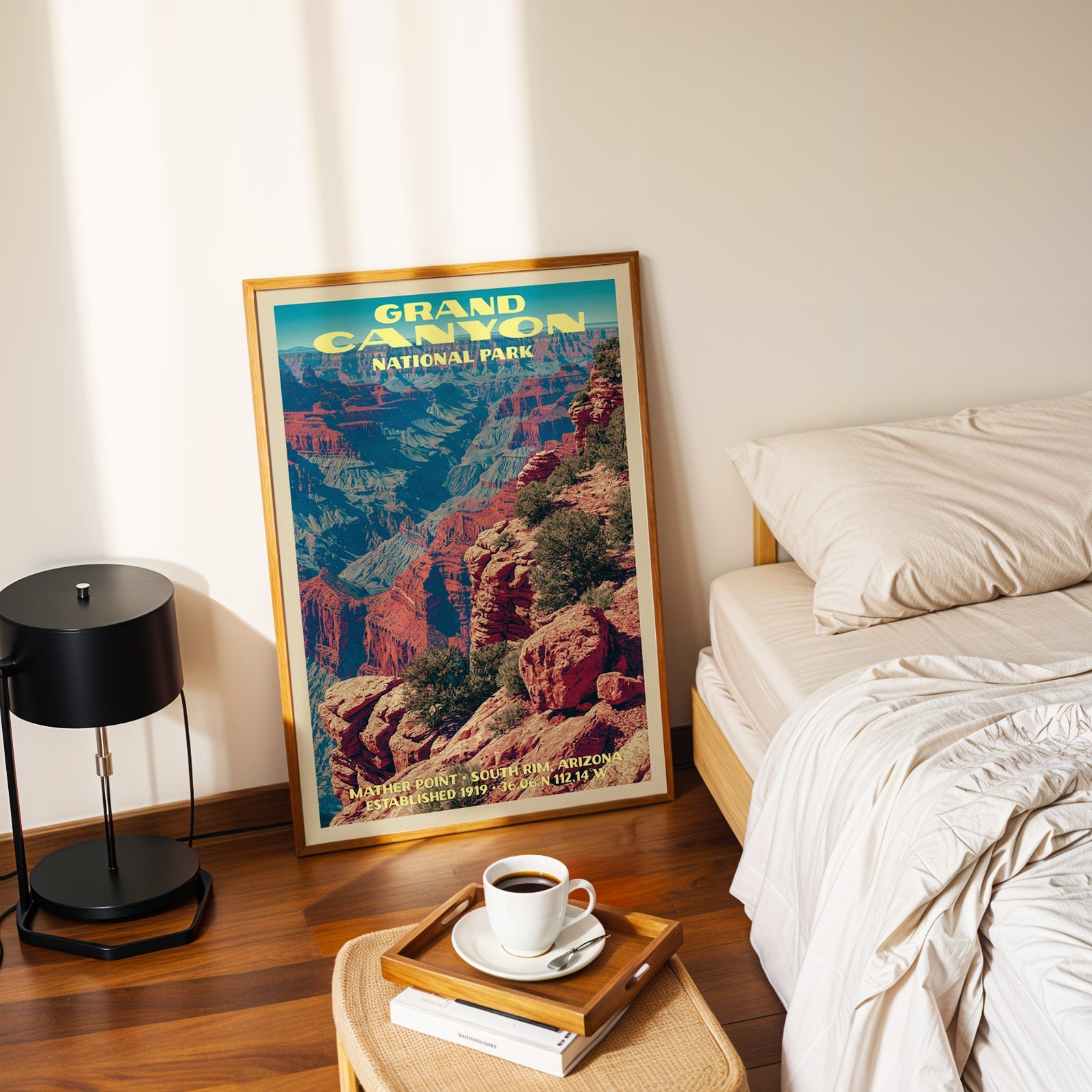 Mather Point South Rim poster in a gold frame on the floor beside a made bed and a black table lamp