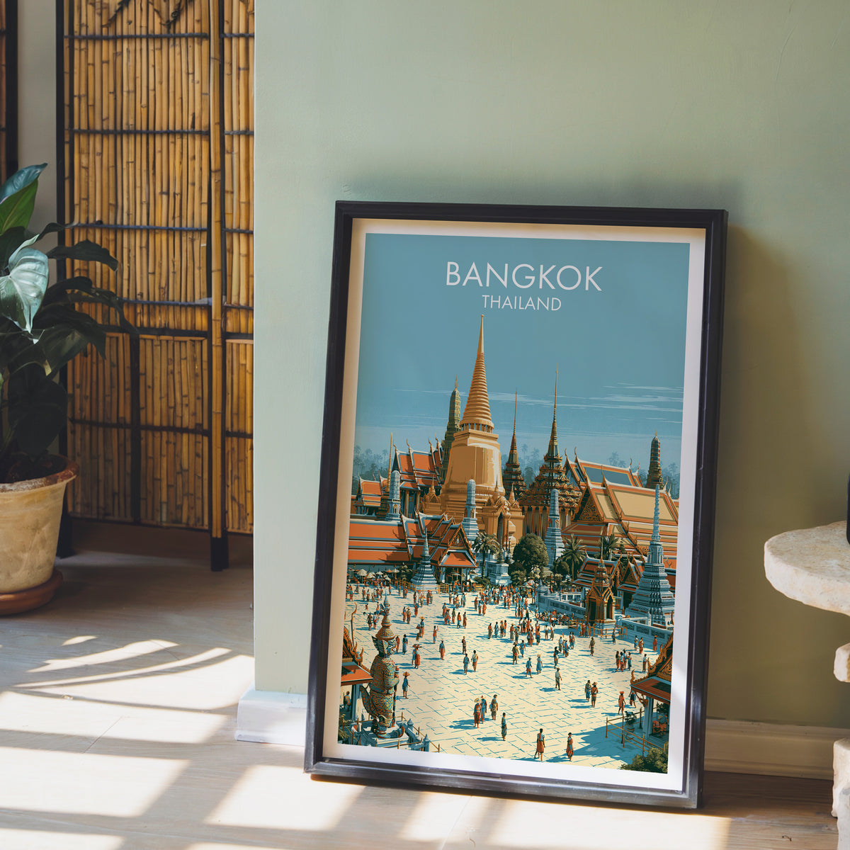 Grand Palace travel print in a black frame leaning against a sage green wall beside a bamboo screen