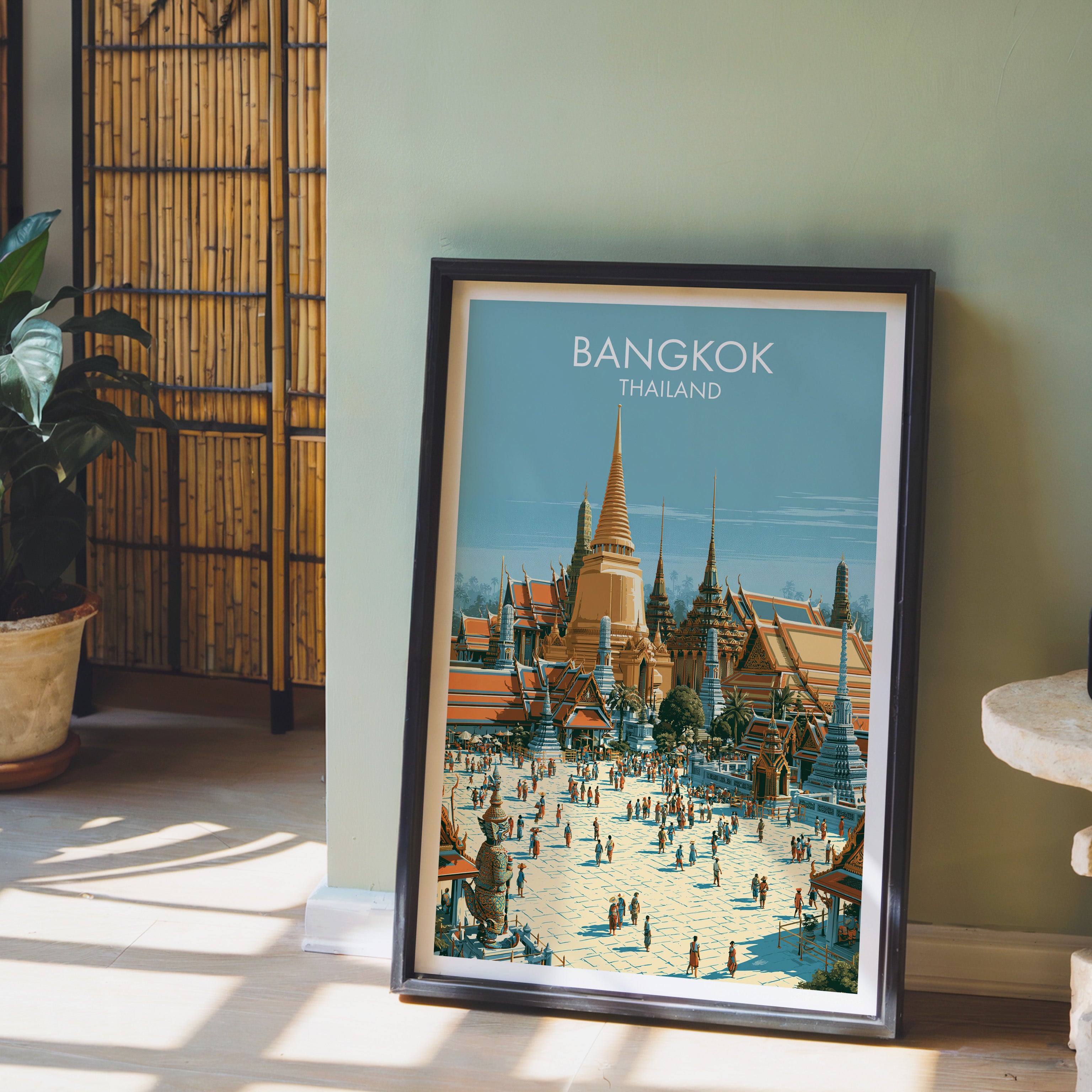 Grand Palace Bangkok Thailand wall art in a black frame leaning against a sage green wall beside a bamboo screen
