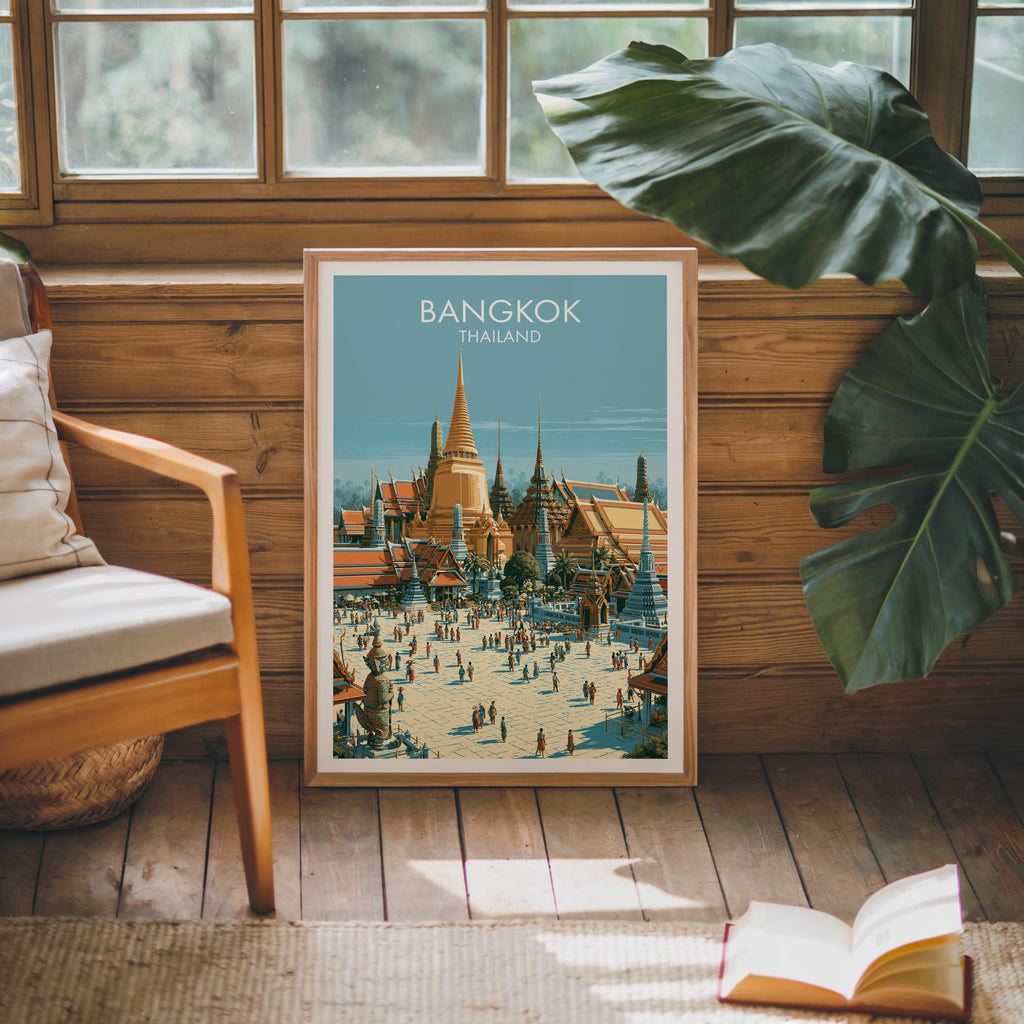 Framed Grand Palace Bangkok Thailand poster leaning against a timber cabin wall with monstera leaves and an open book