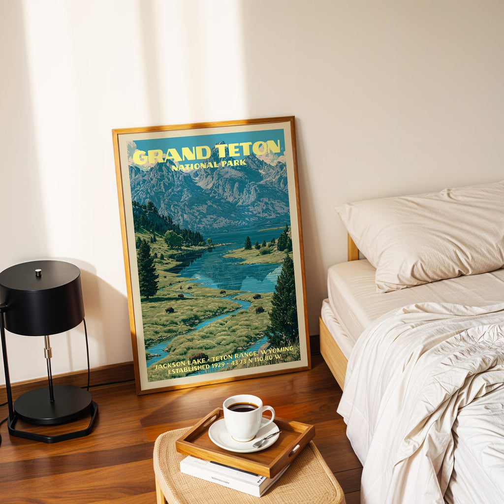 Jackson Lake Teton Range poster in a gold frame on the floor beside a made bed and a black table lamp