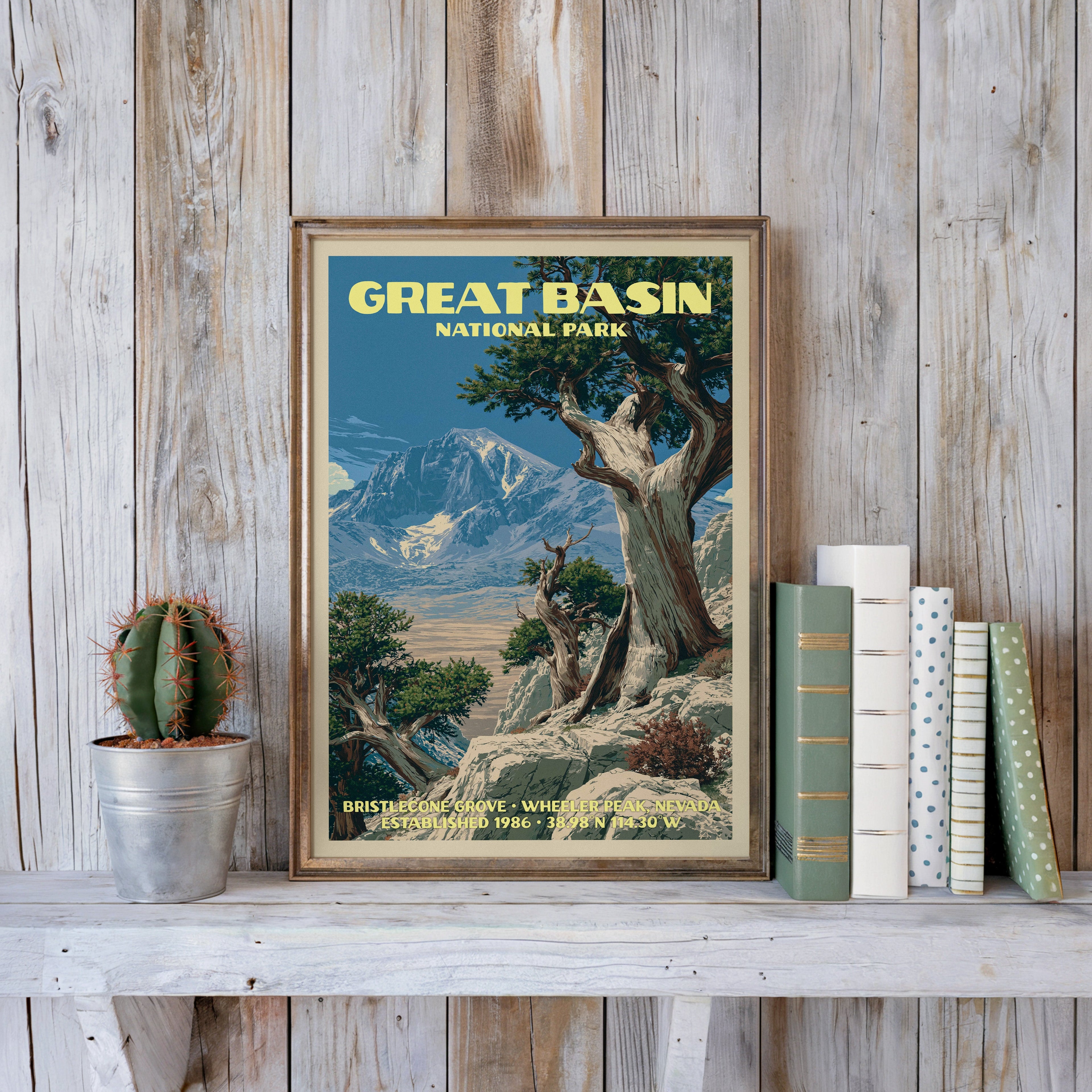 Great Basin vintage poster in a slim gold frame on a whitewashed plank wall beside a tin-potted cactus and pastel books
