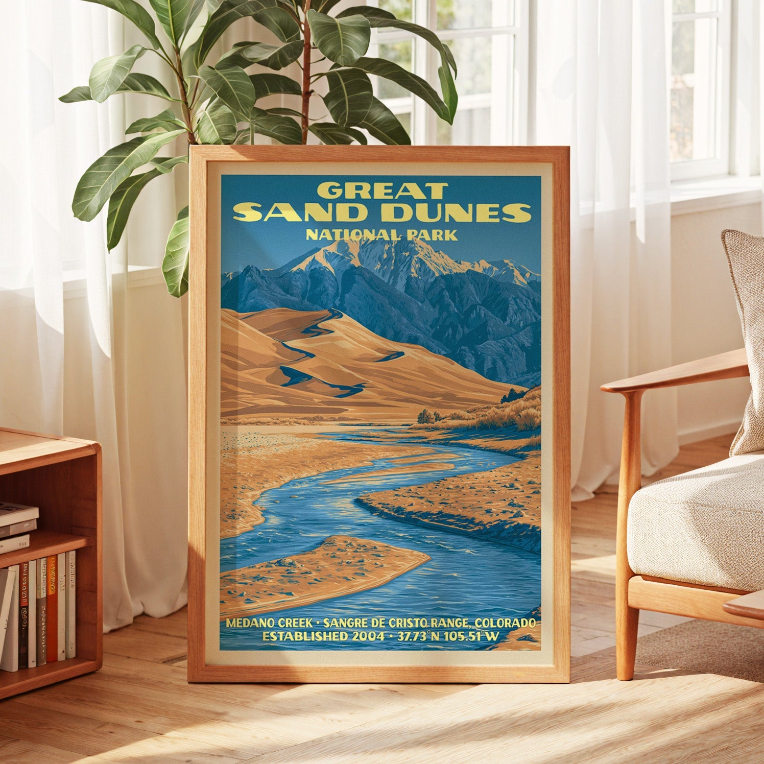 Great Sand Dunes poster in oak, leaning by a sunlit window with sheer curtains and a low bookshelf
