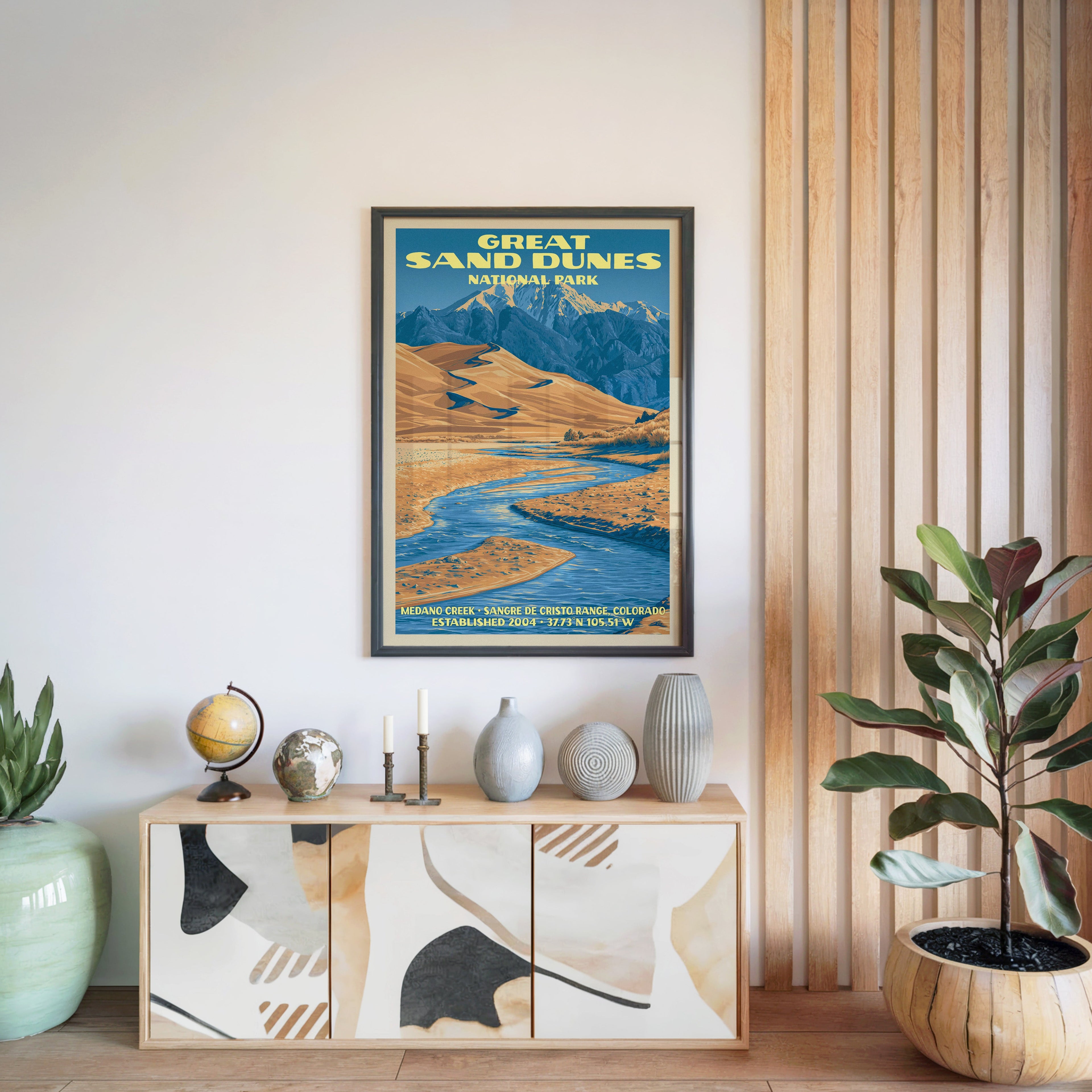 Great Sand Dunes National Park poster in a black frame above a light wood sideboard with a globe and a slatted panel