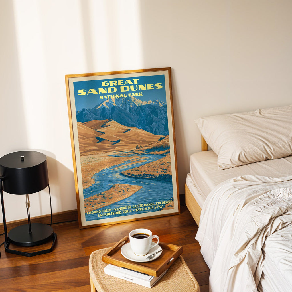 Medano Creek dunes poster in a gold frame on the bedroom floor beside a made bed and a black table lamp