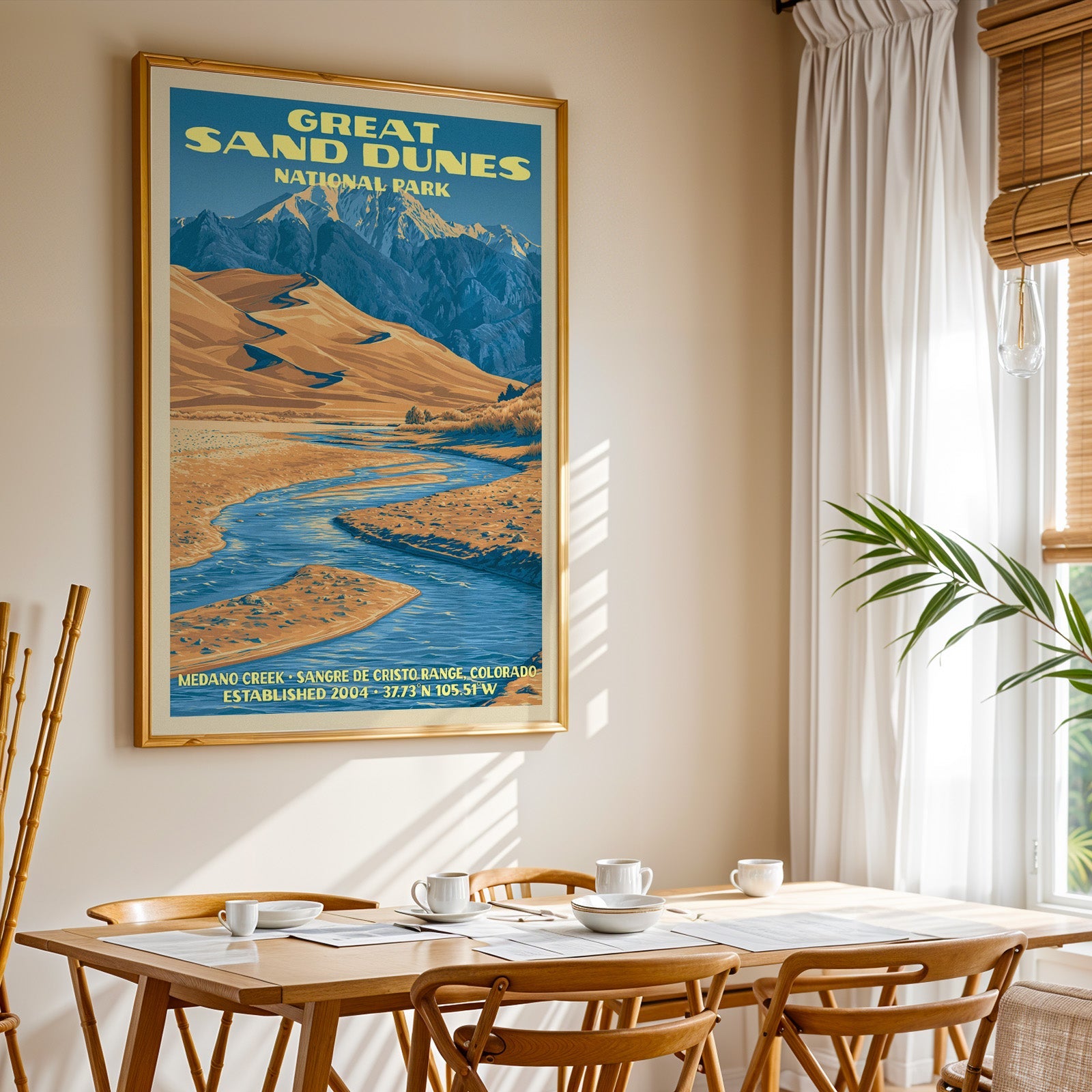Great Sand Dunes National Park print in a gold frame above a light oak dining table by a curtained window
