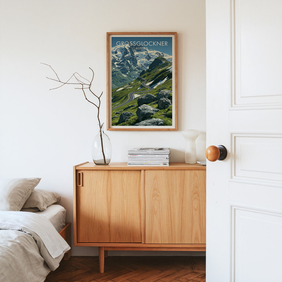 Grossglockner mountain pass print, oak frame above a light oak sideboard with bare branches in a glass vase