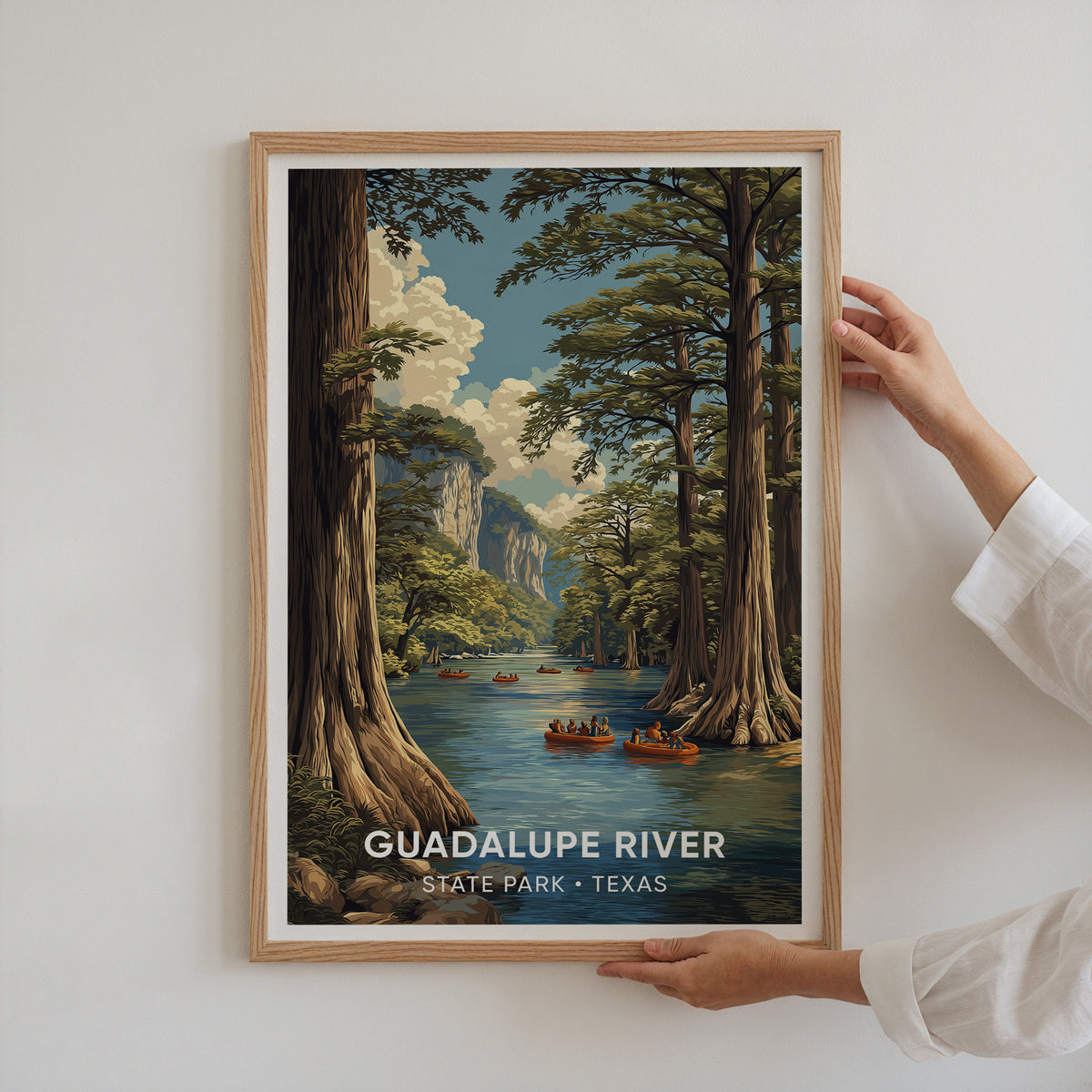 Two hands holding an oak-framed Guadalupe River State Park poster against a plain white wall