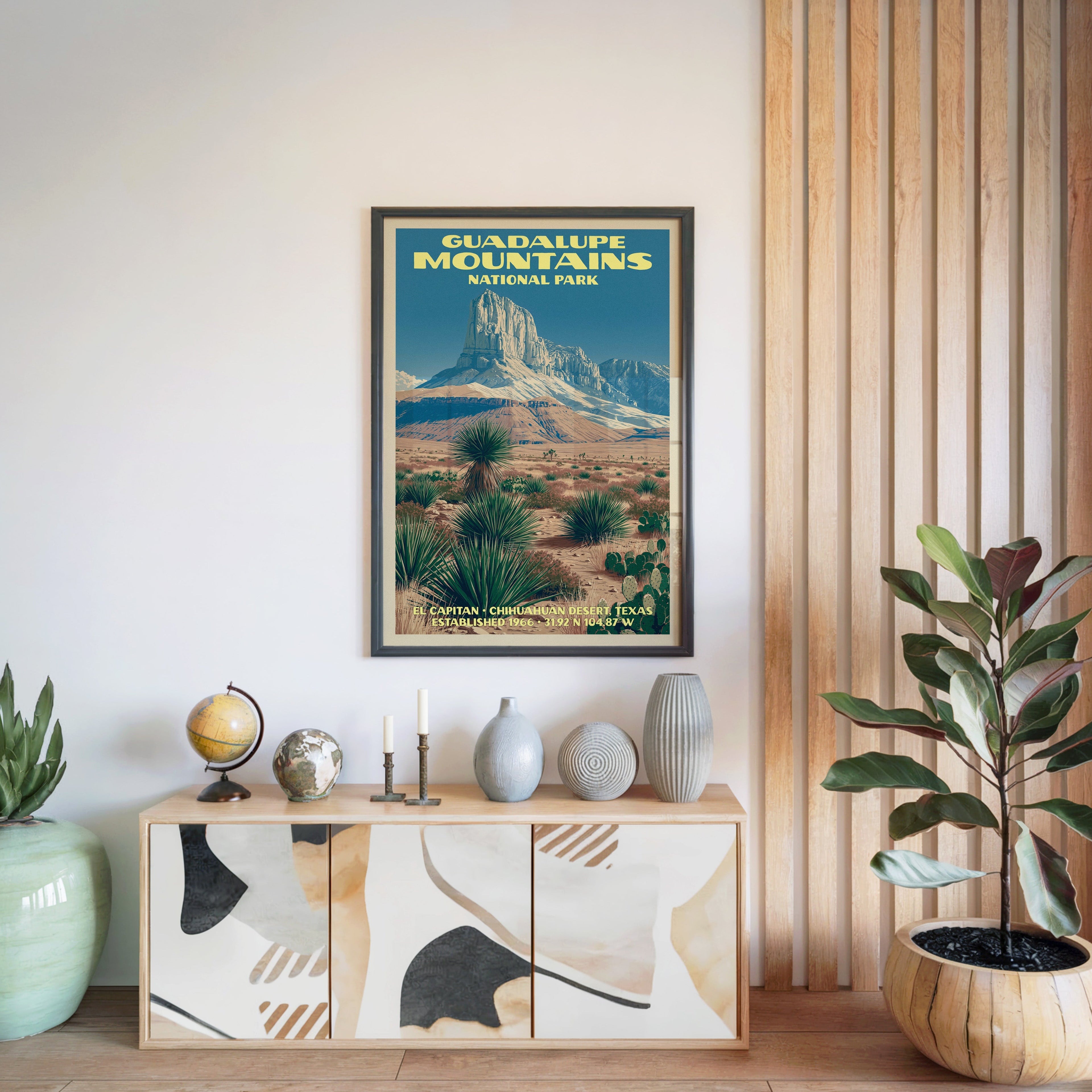 Guadalupe Mountains National Park poster in a black frame above a light wood sideboard with a globe and candlesticks