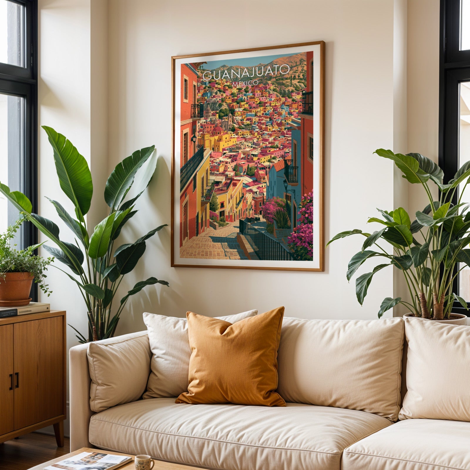Guanajuato travel print in an oak frame above a cream sofa with a burnt-orange cushion and tropical plants