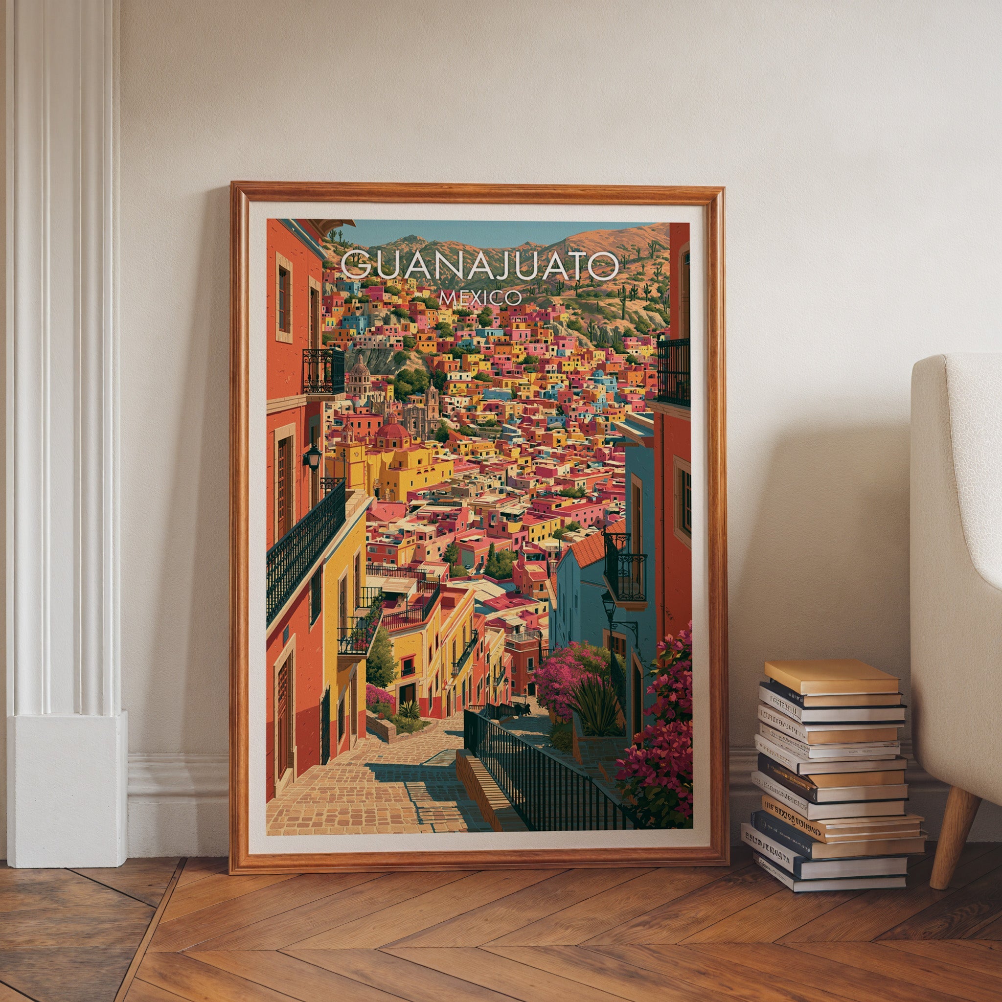 Guanajuato lane print in a walnut frame on a herringbone floor with stacked books and a pale armchair