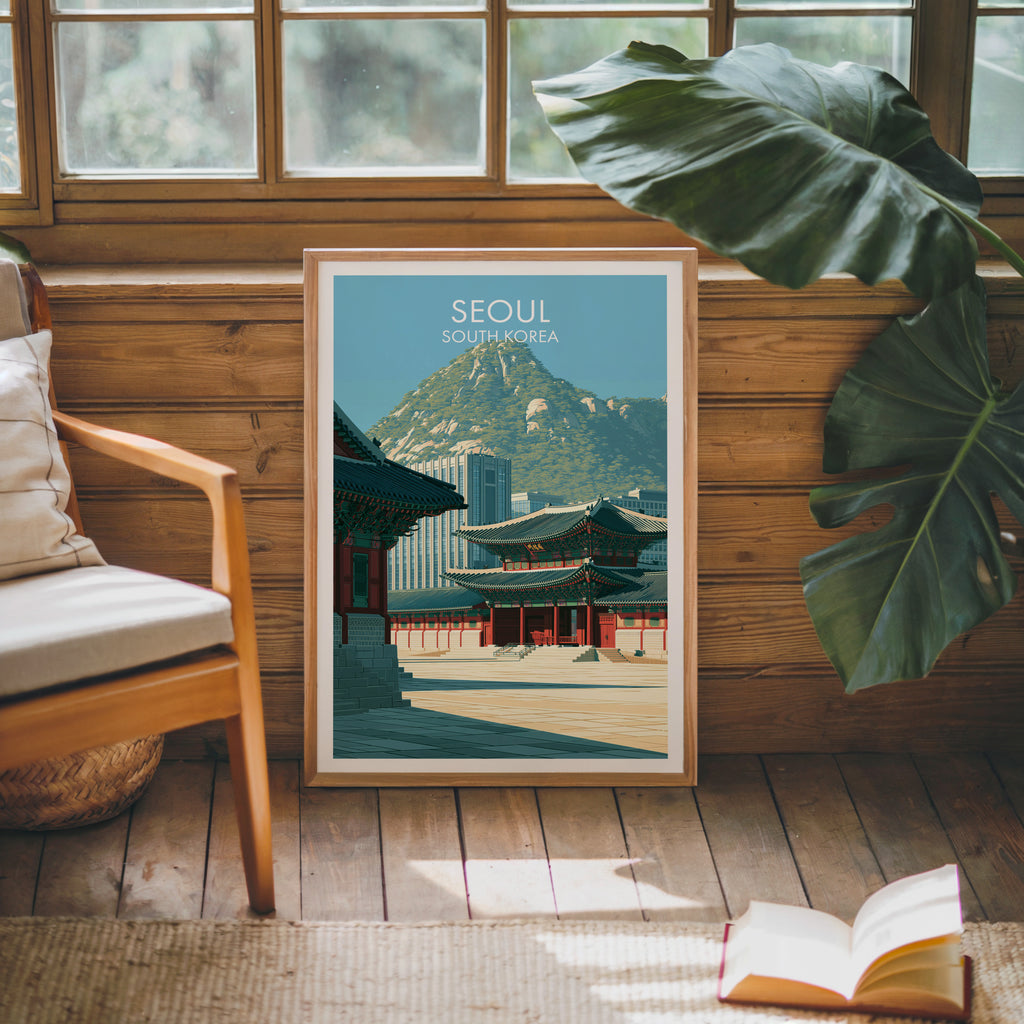 Framed Gyeongbokgung Palace Seoul poster leaning against a timber cabin wall with monstera leaves and an open book