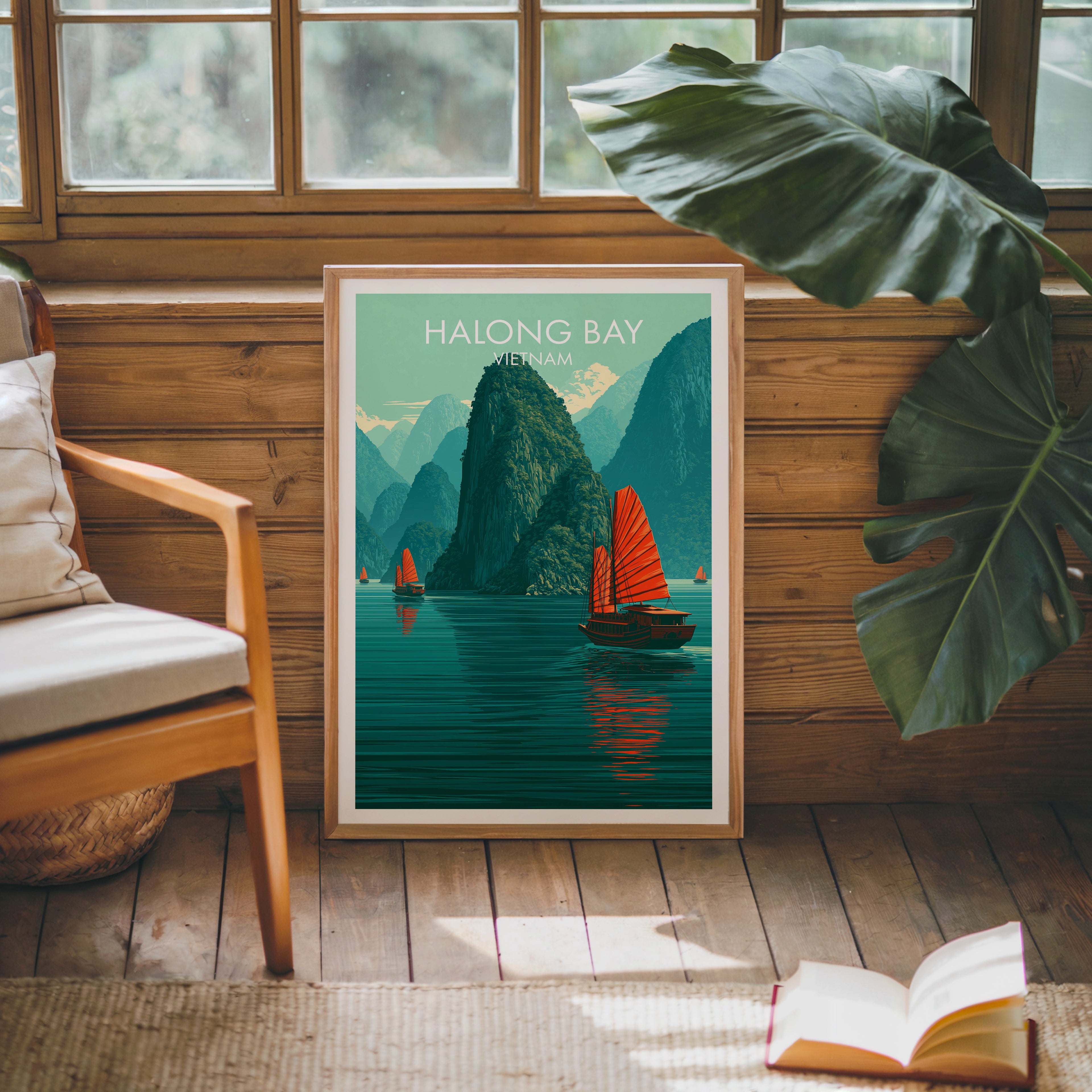 Framed Halong Bay Vietnam poster leaning against a timber cabin wall with monstera leaves and an open book