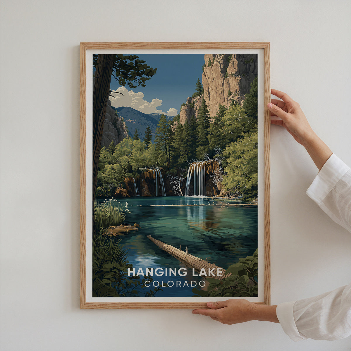 Two hands holding the Hanging Lake print in an oak frame flat against a white wall