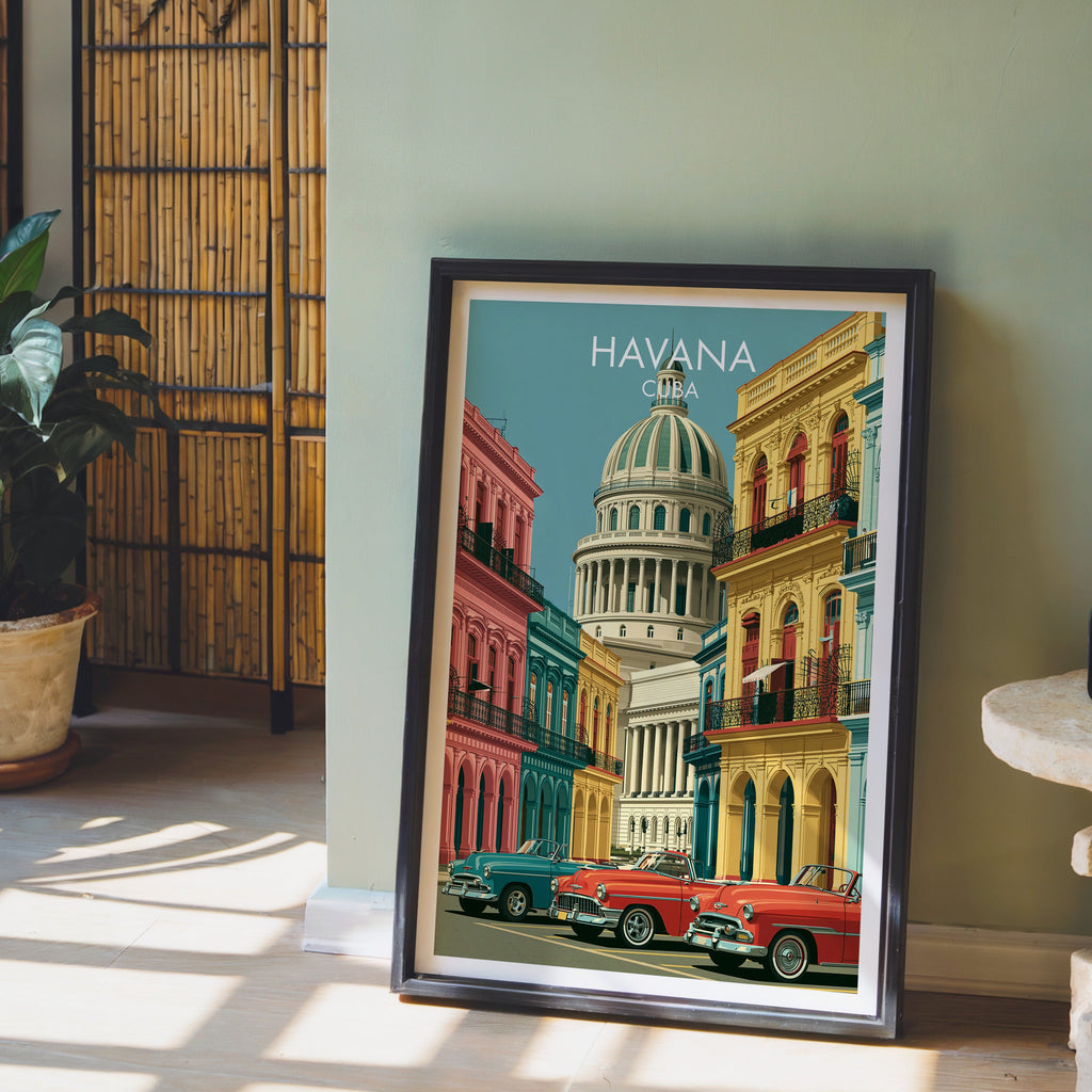 Classic Cuban cars print in a black frame leaning on pale wood floor by a sage-green wall, bamboo screen and plant