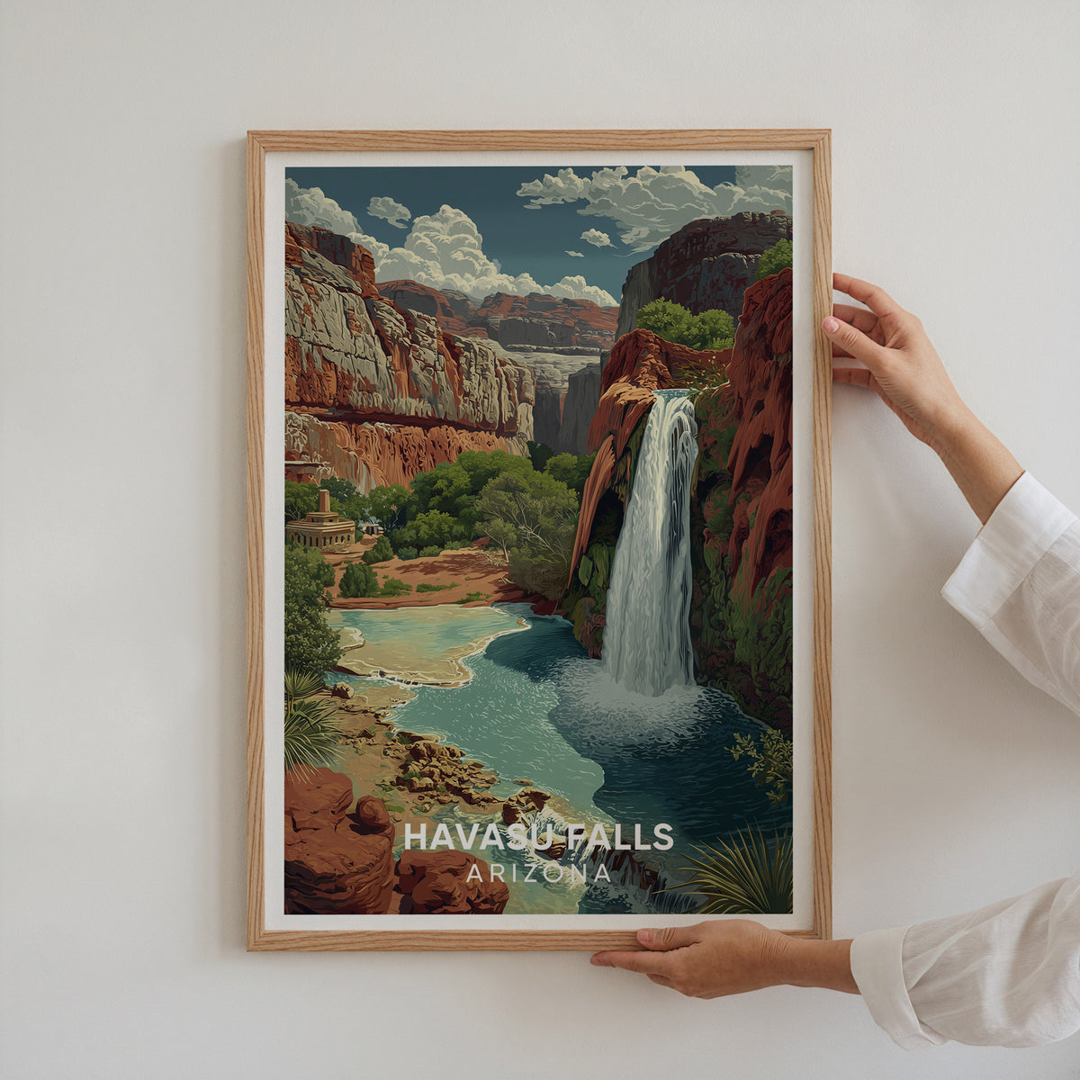 Two hands holding the Havasu Falls print in an oak frame against a white wall