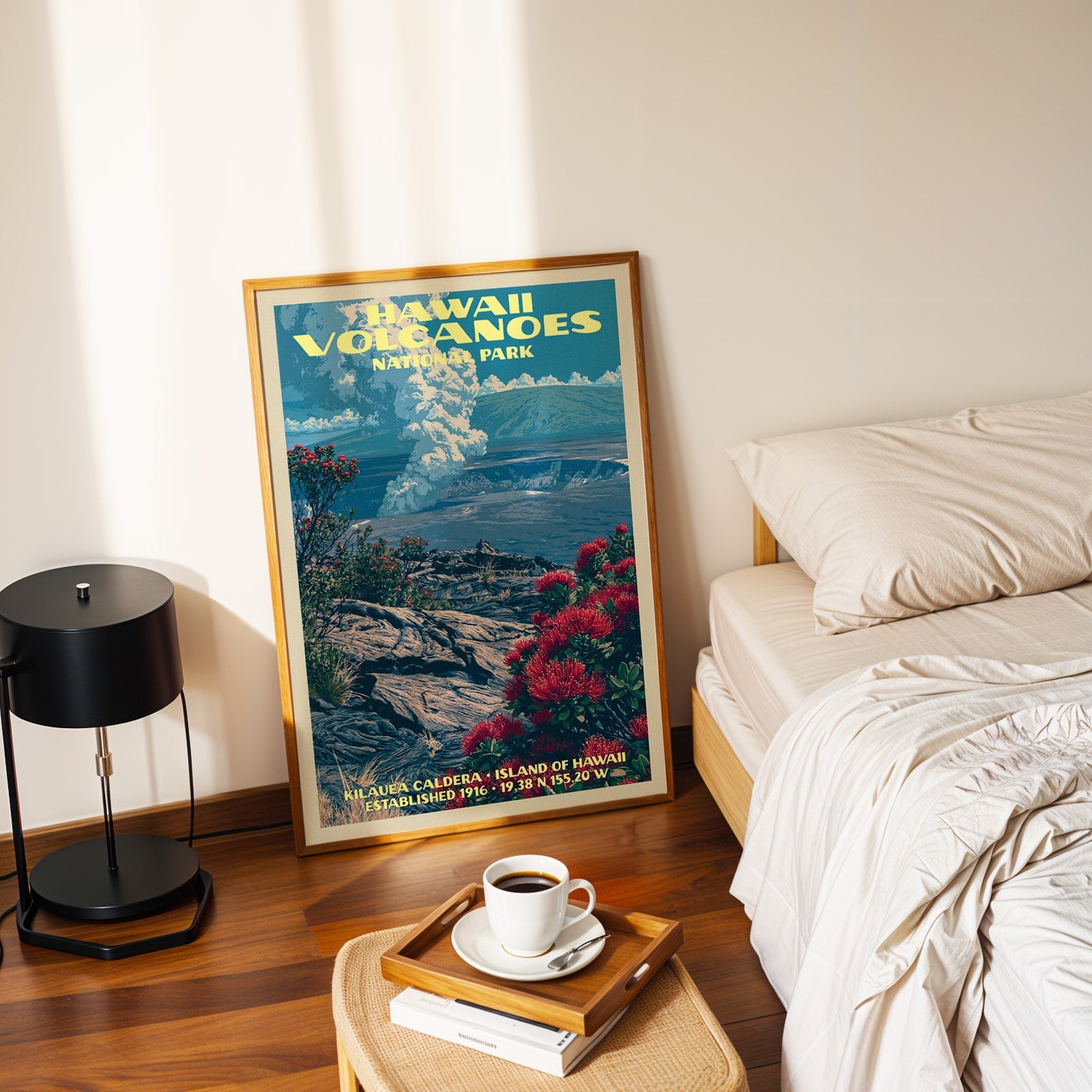 Kilauea lehua poster in a gold frame on the bedroom floor beside a made bed and a black table lamp