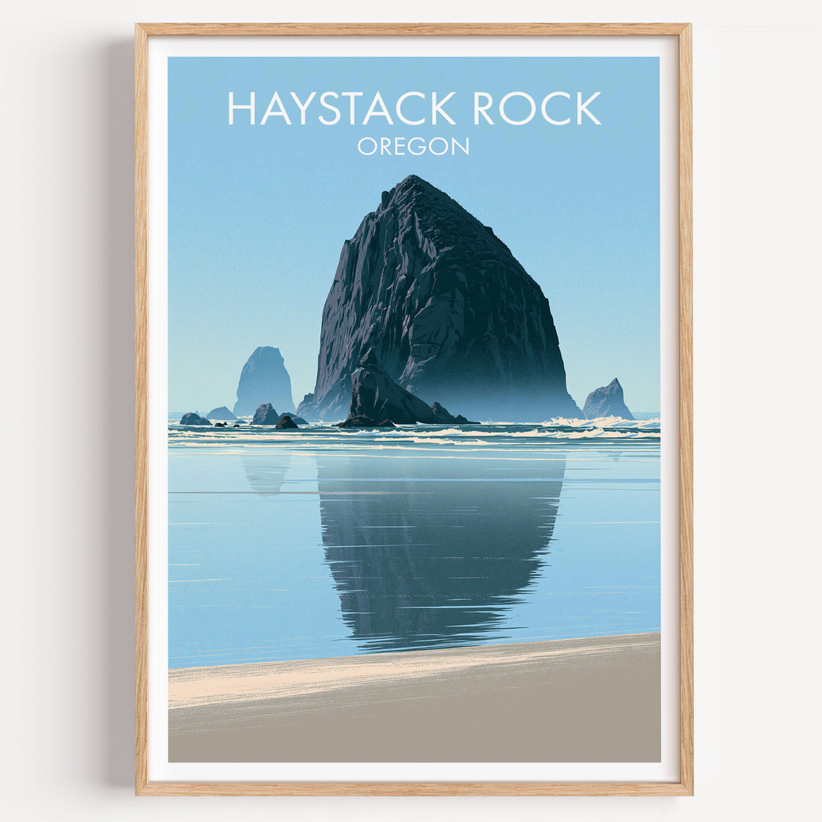 Haystack Rock travel poster in a pale oak frame on a bare white wall, shot straight on with one soft shadow