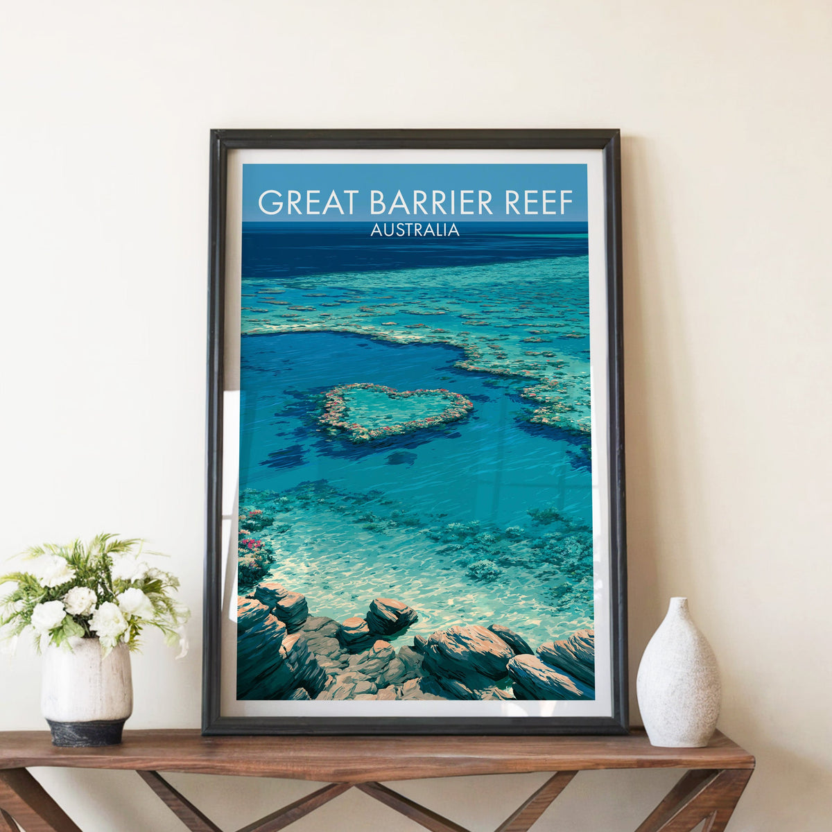 Great Barrier Reef poster in a black frame on a walnut console with white peonies and a tall stone vase