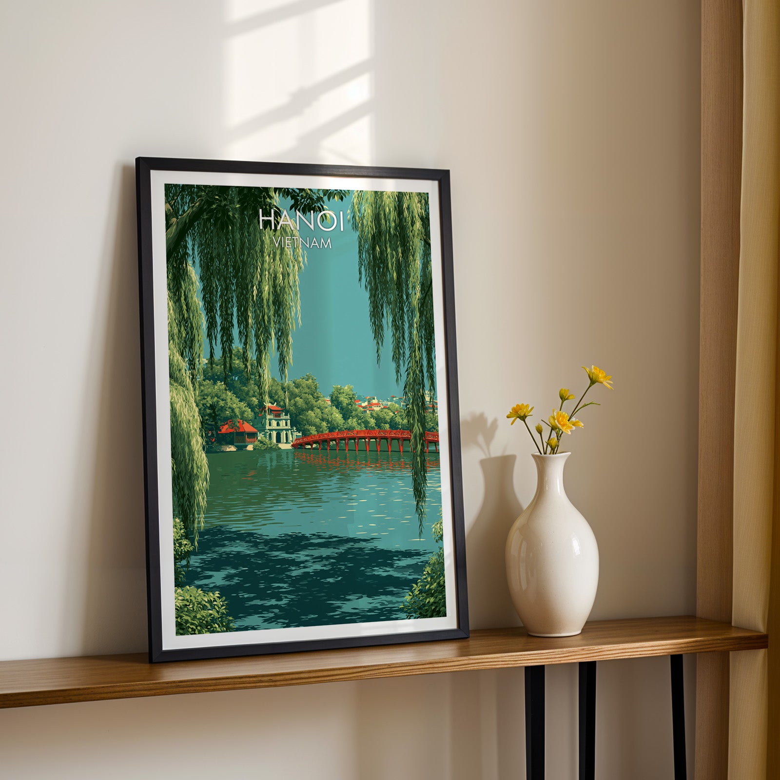 Black framed Hoan Kiem Lake Hanoi Vietnam print on a narrow hallway console in sunlight, styled with yellow flowers