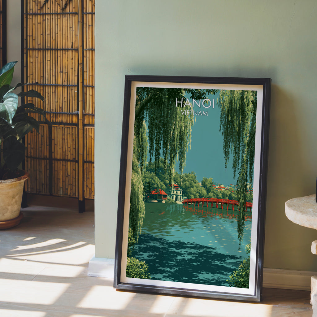 Hoan Kiem Lake Hanoi Vietnam wall art in a black frame leaning against a sage green wall beside a bamboo screen