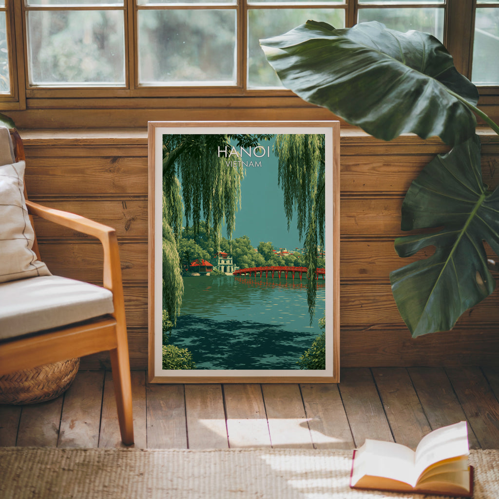 Framed Hoan Kiem Lake Hanoi Vietnam poster leaning against a timber cabin wall with monstera leaves and an open book