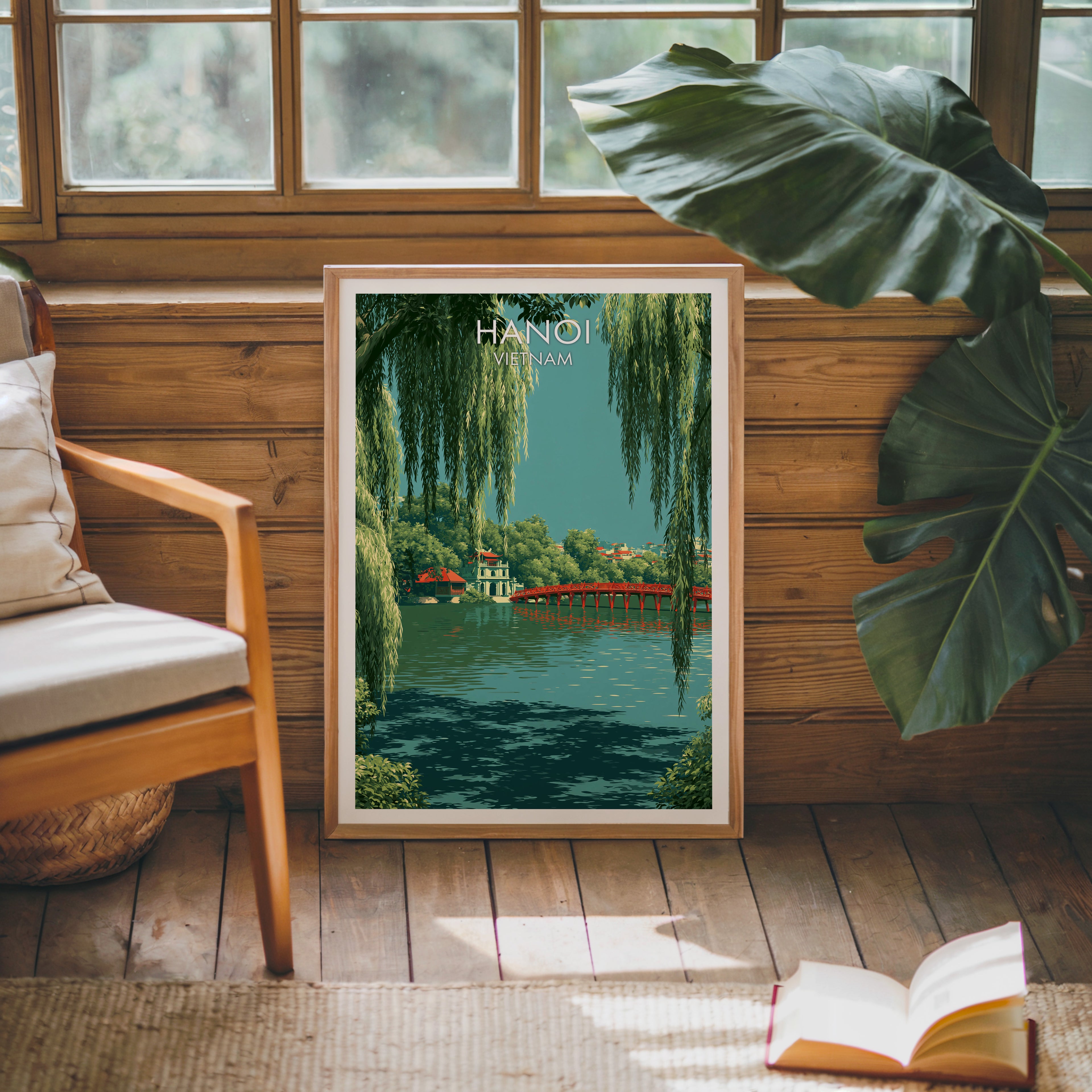 Framed Hoan Kiem Lake Hanoi Vietnam poster leaning against a timber cabin wall with monstera leaves and an open book