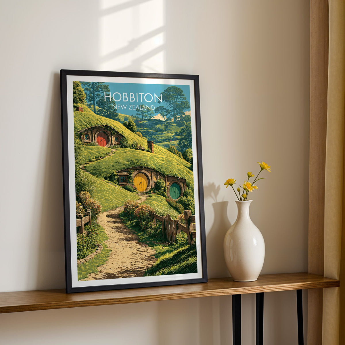 Round door hillside print, black frame on a wood shelf with yellow daisies on a sunlit cream wall