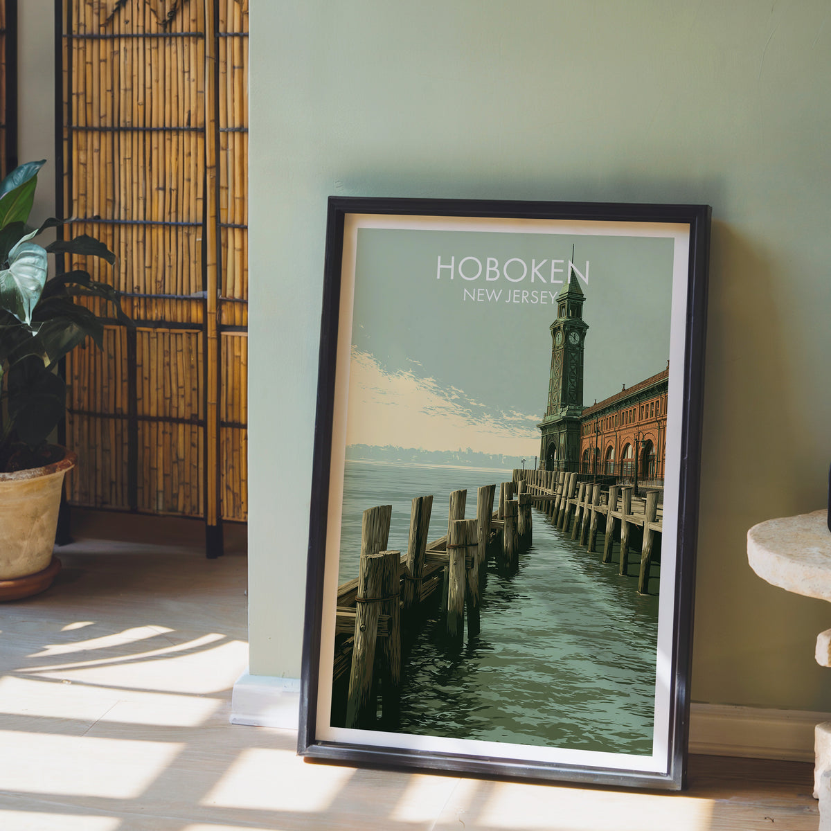 Hudson River pier print in a black frame by a sage green wall, bamboo screen, potted orchid and stone table.