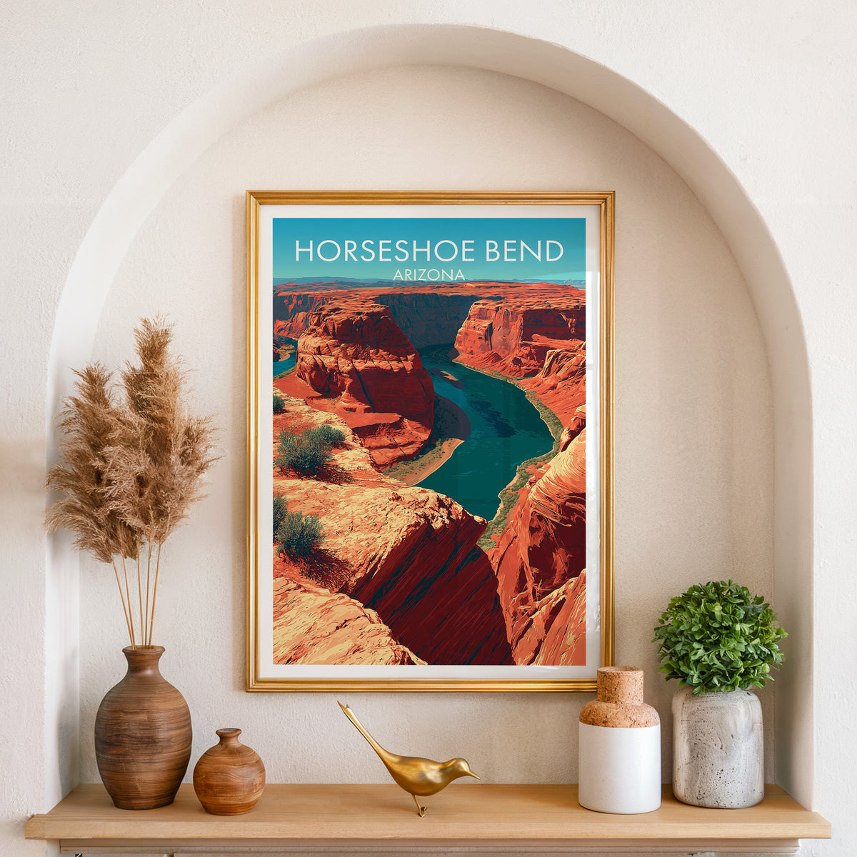 Desert river canyon artwork in a gold frame set in an arched wall niche with pampas grass and a brass bird