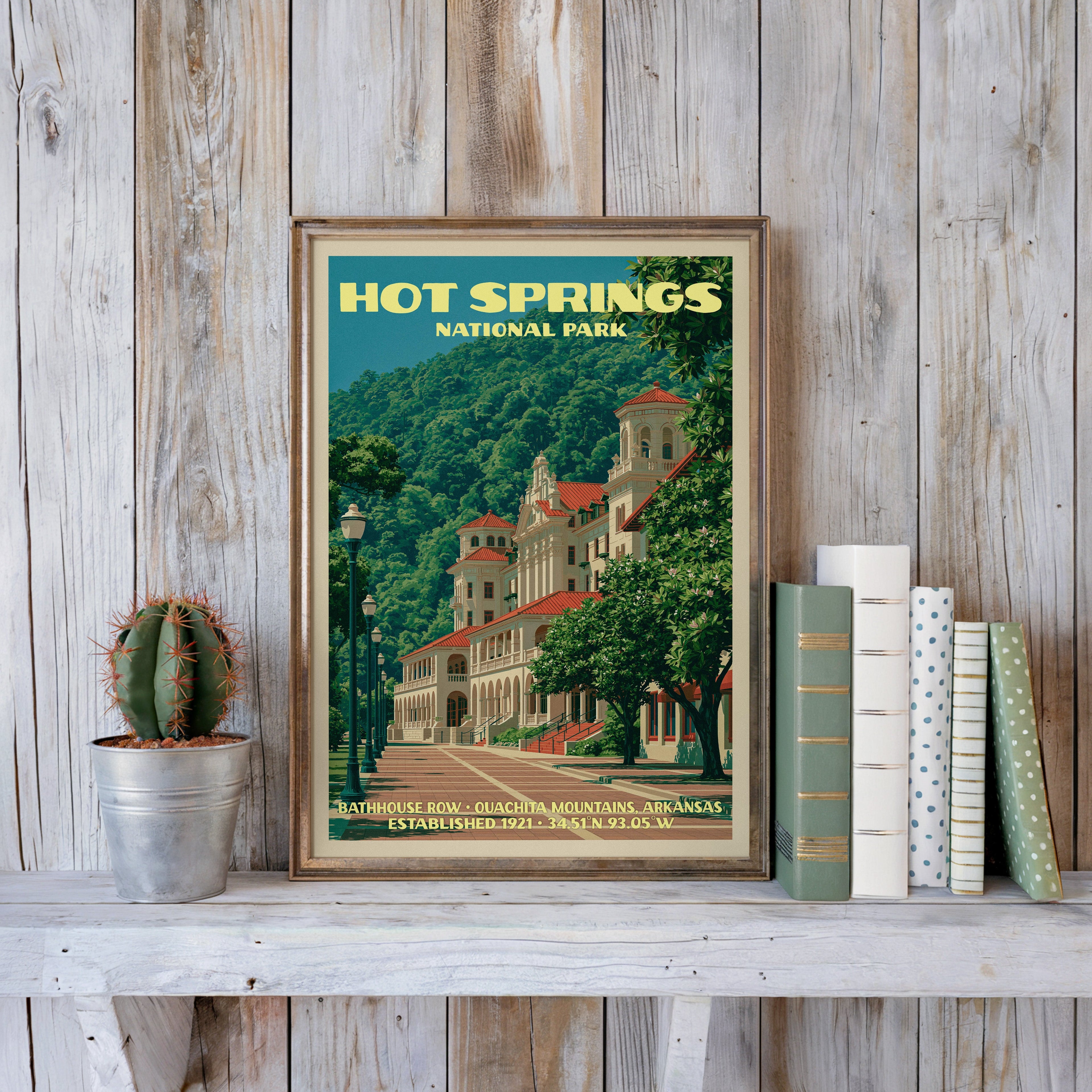 Bathhouse Row poster in a slim gold frame on a whitewashed plank wall beside a tin-potted cactus and books