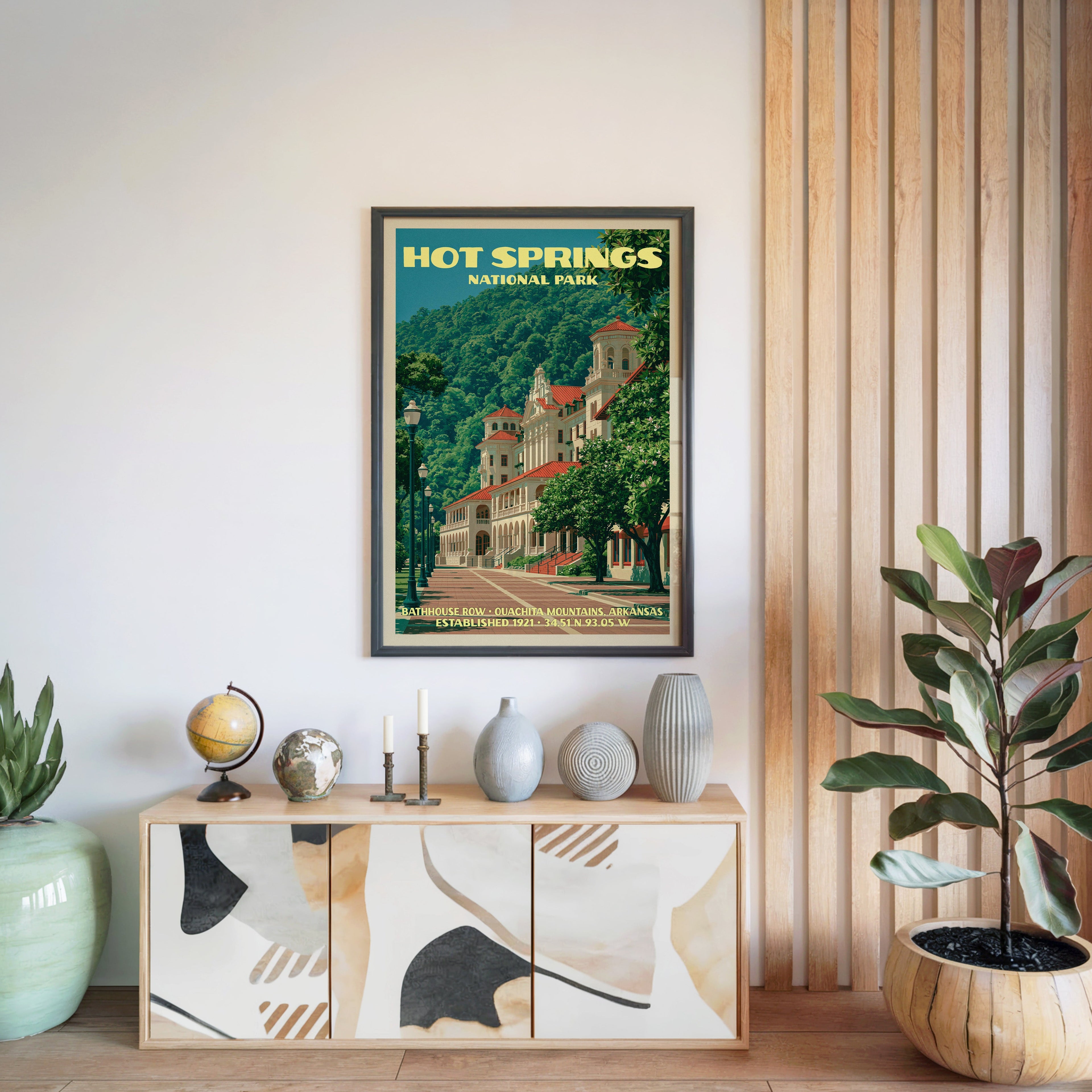 Hot Springs National Park poster in a black frame above a light wood sideboard with a globe and a candlestick