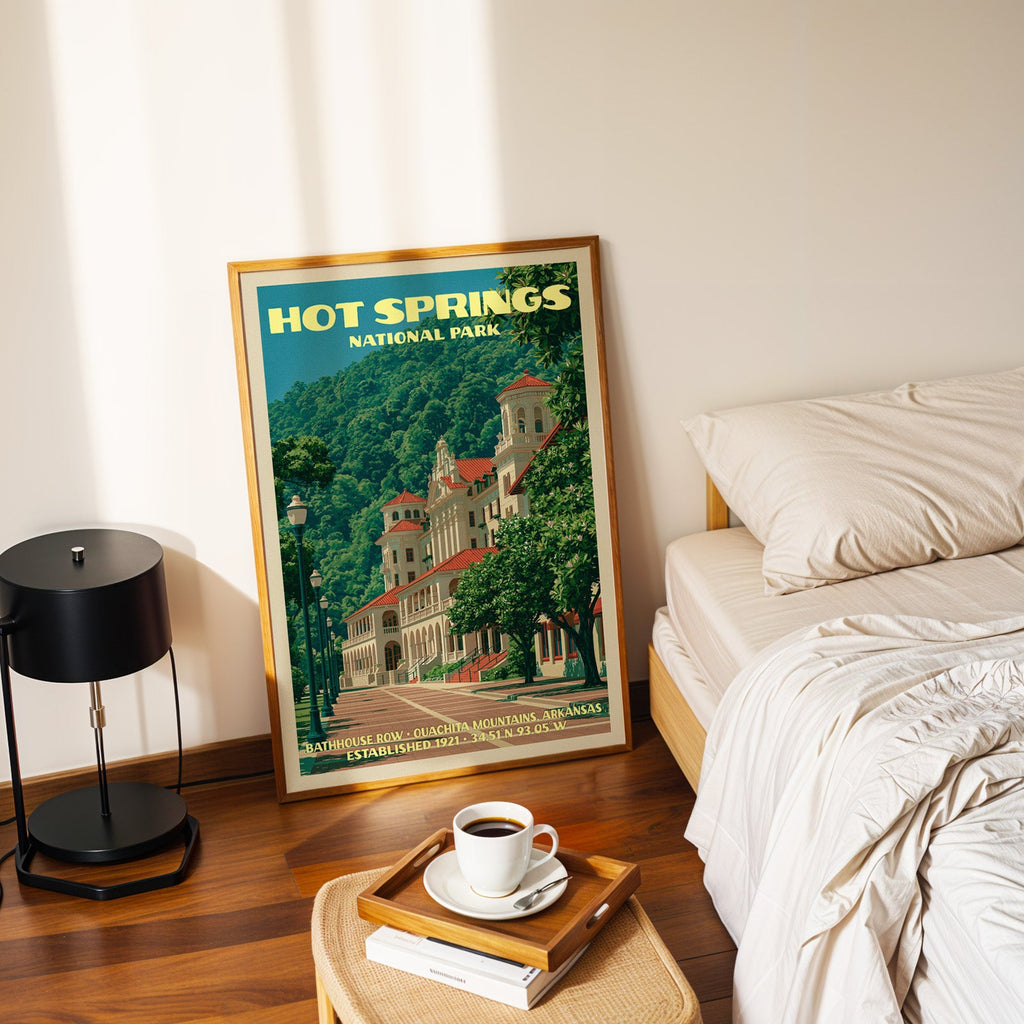Bathhouse Row Arkansas poster in a gold frame on the bedroom floor beside a made bed and a black table lamp