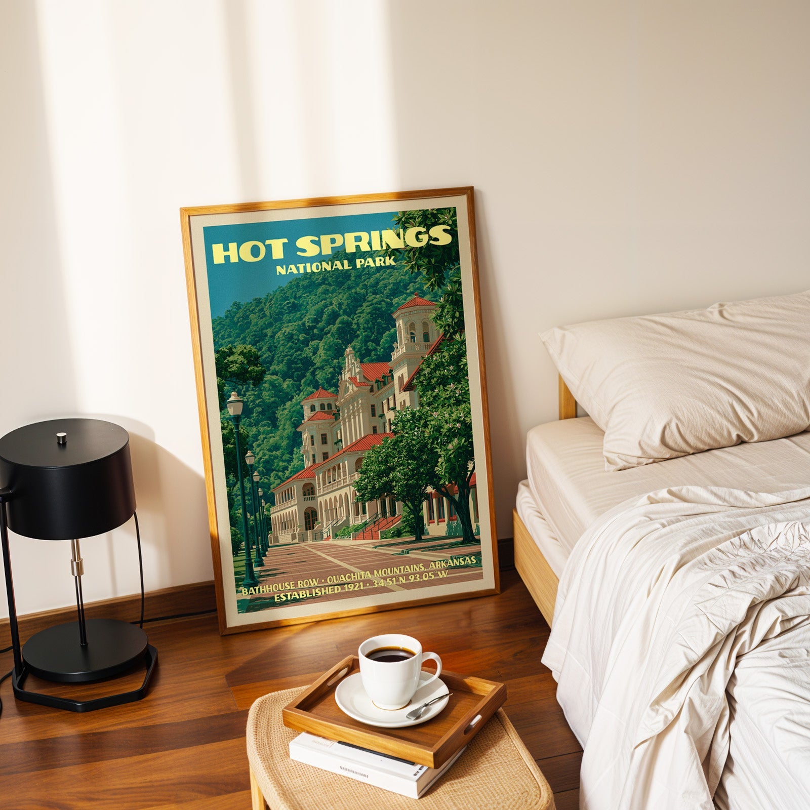 Bathhouse Row Arkansas poster in a gold frame on the bedroom floor beside a made bed and a black table lamp