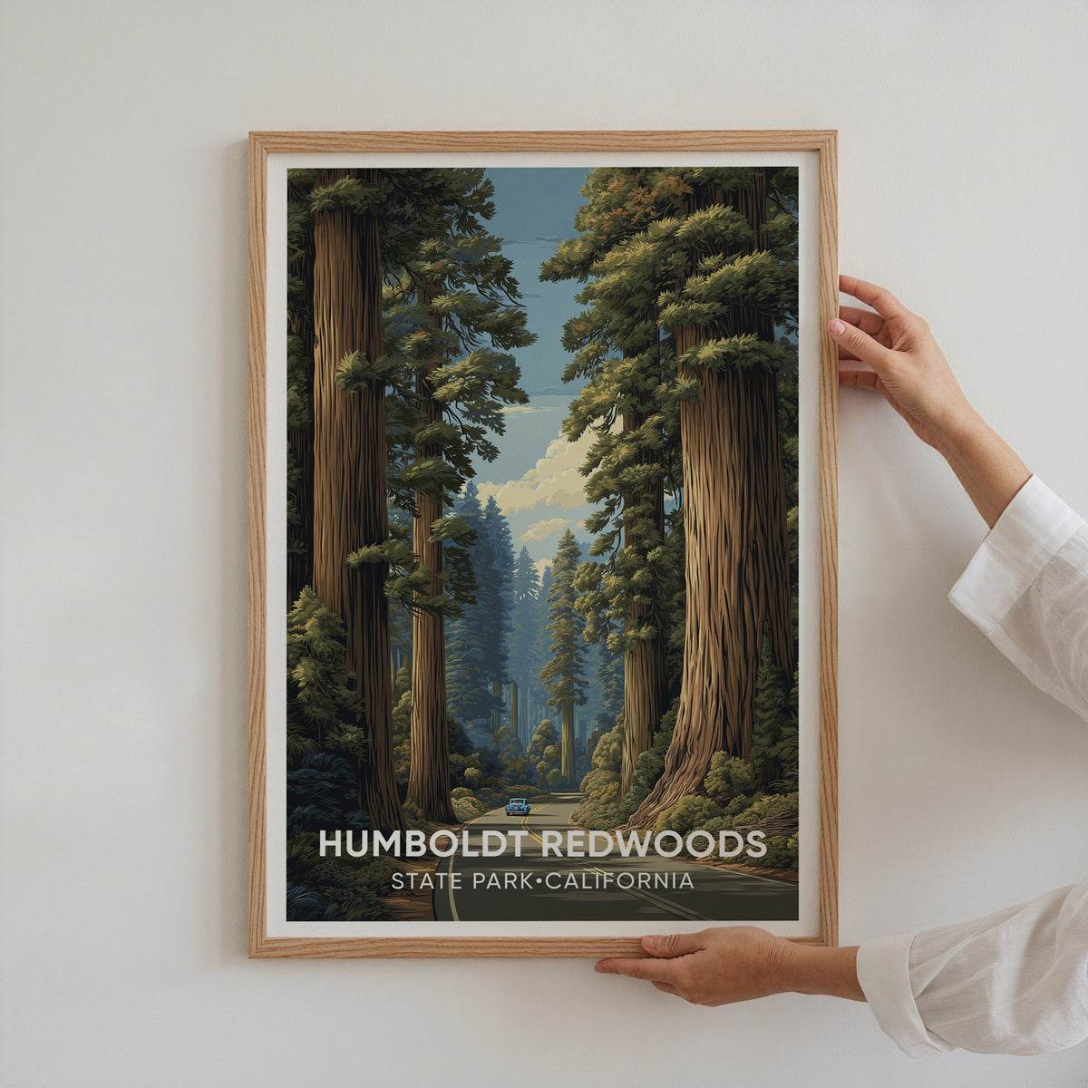 Two hands holding the Humboldt Redwoods print in an oak frame against a white wall
