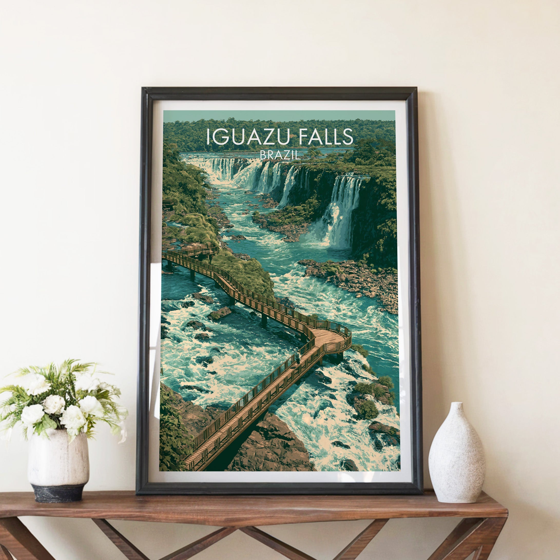 Iguazu boardwalk print in a black frame on a brown console table with white flowers in a ceramic vase
