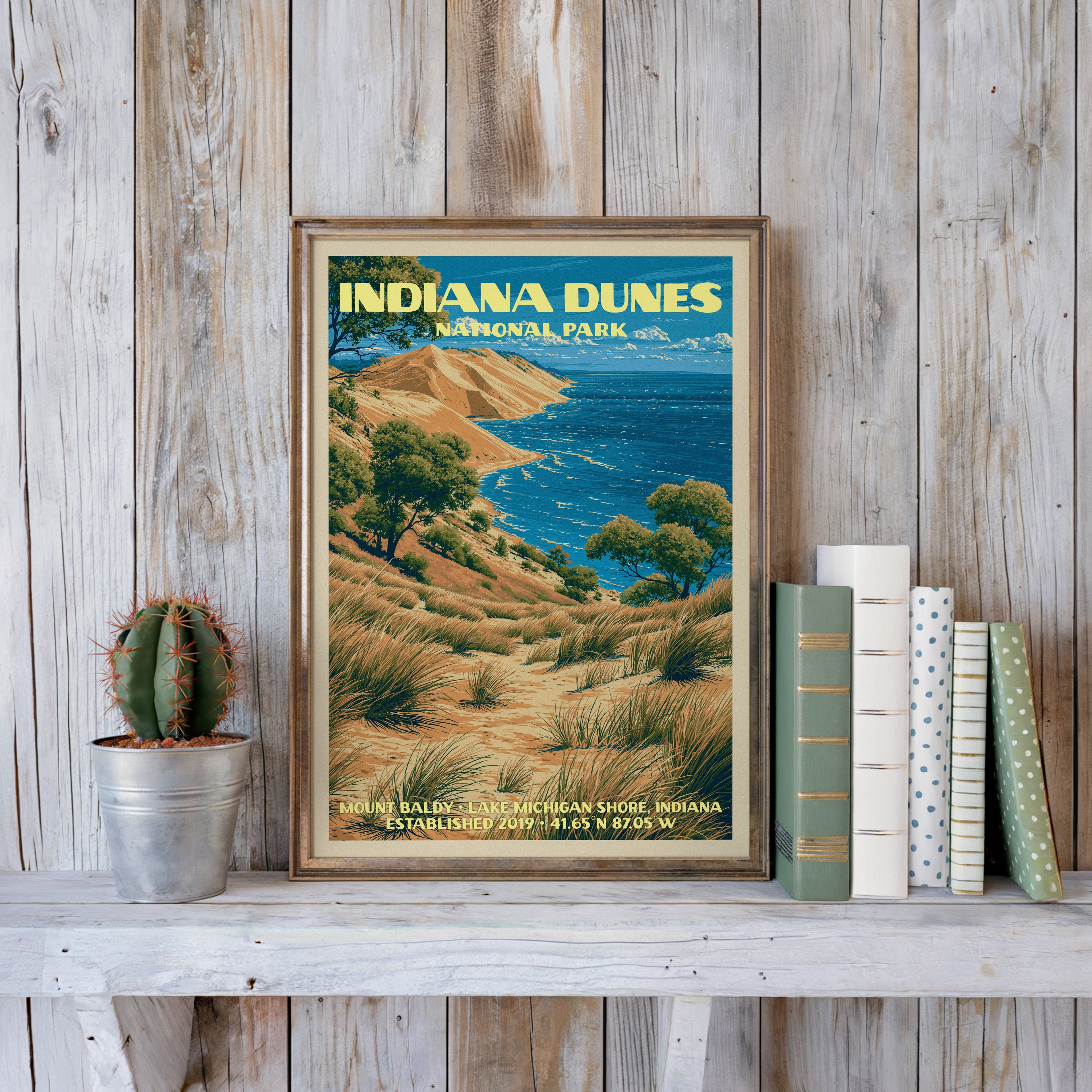 Mount Baldy poster in a slim gold frame on a whitewashed plank wall beside a tin-potted cactus and pastel books