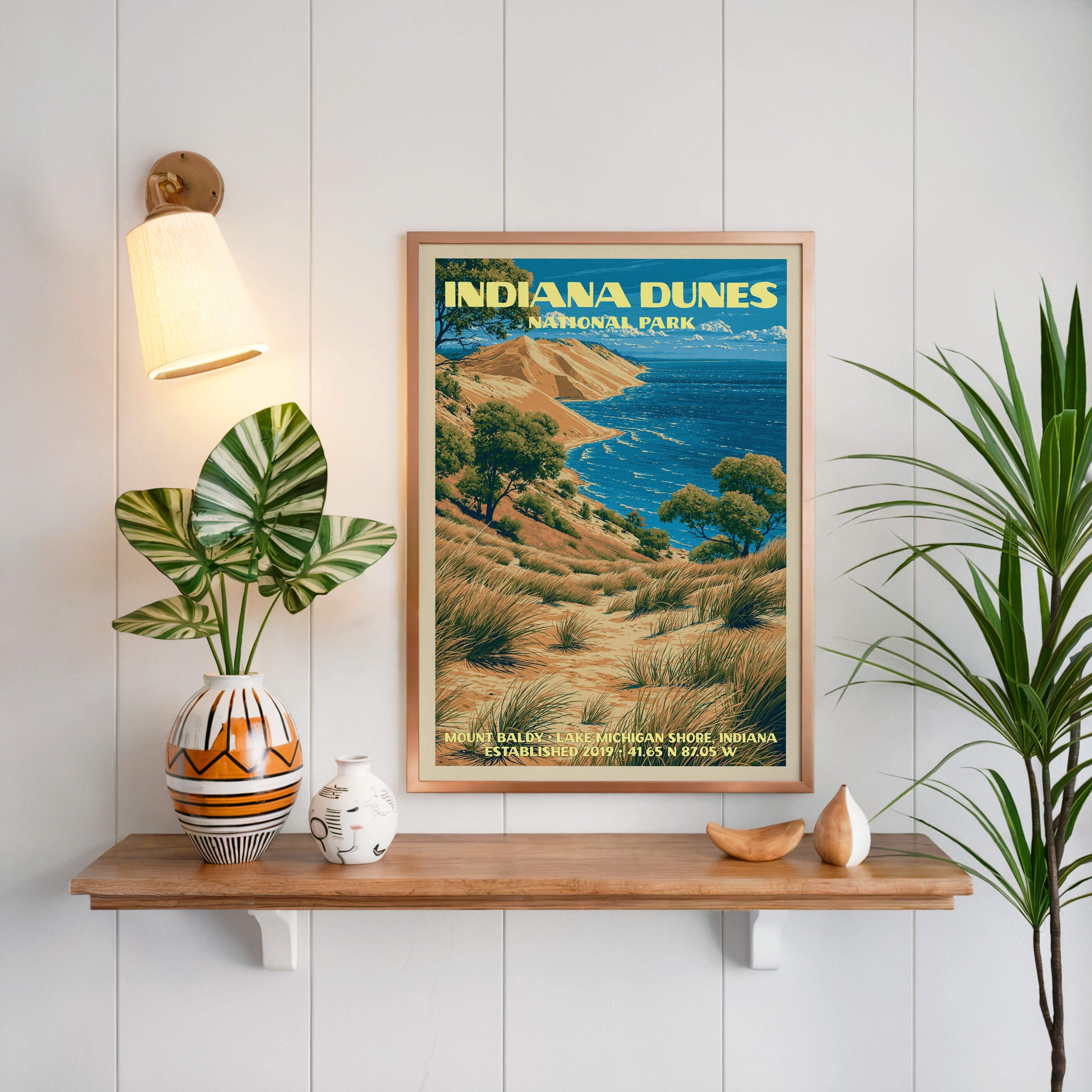 Indiana Dunes print framed on white panelling above a floating oak shelf with a patterned vase and brass sconce