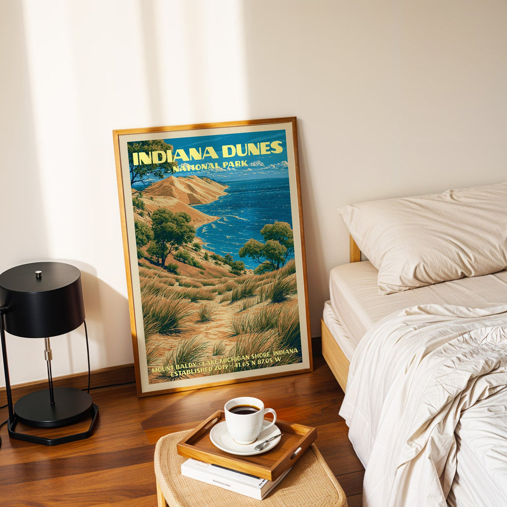 Mount Baldy dune poster in a gold frame on the bedroom floor beside a made bed and a black table lamp